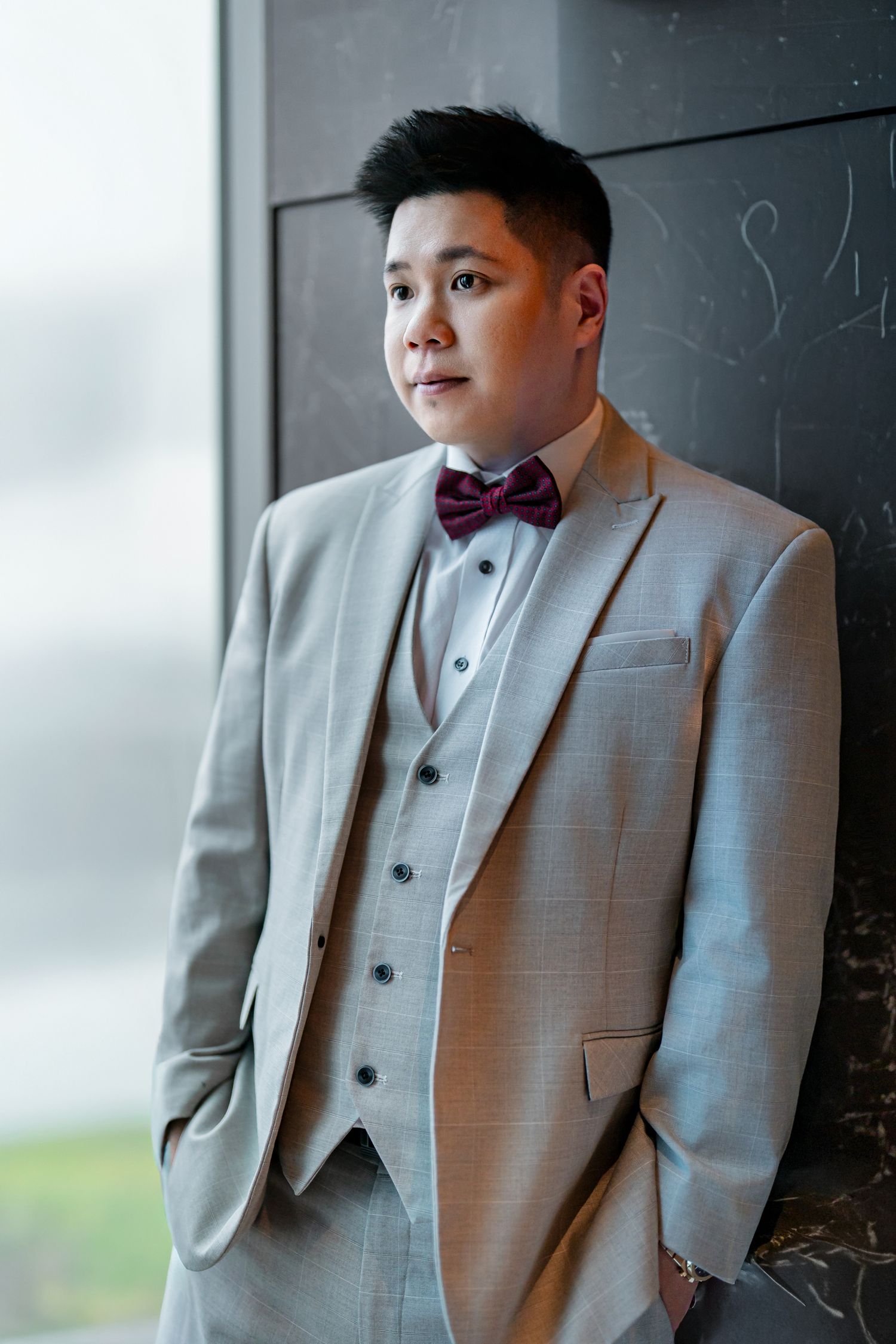 A person in a light gray three-piece suit and bowtie poses against a dark background.