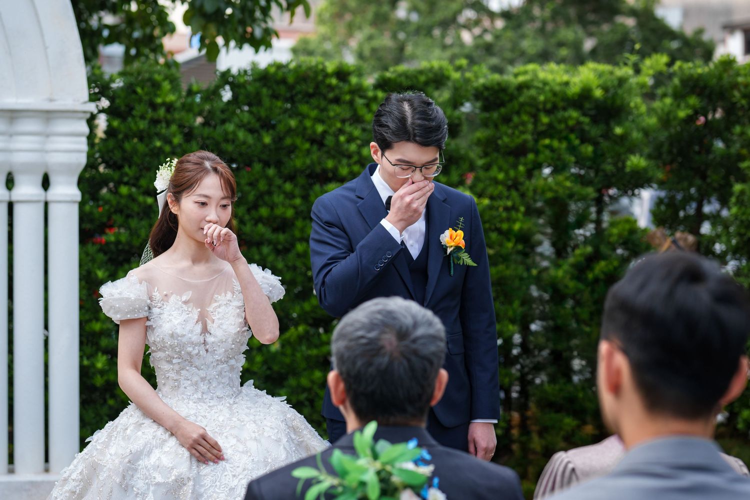 A couple shares an emotional moment during their outdoor wedding ceremony under a white gazebo.