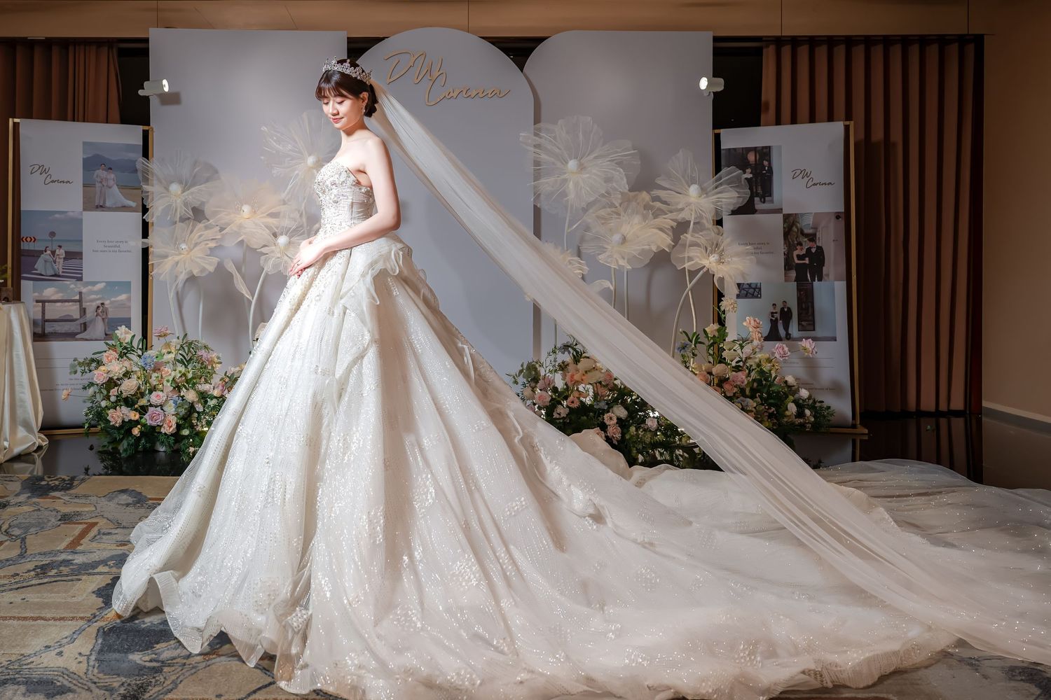 Elegant bride in a stunning white ball gown with long veil and embroidered train at a wedding venue.