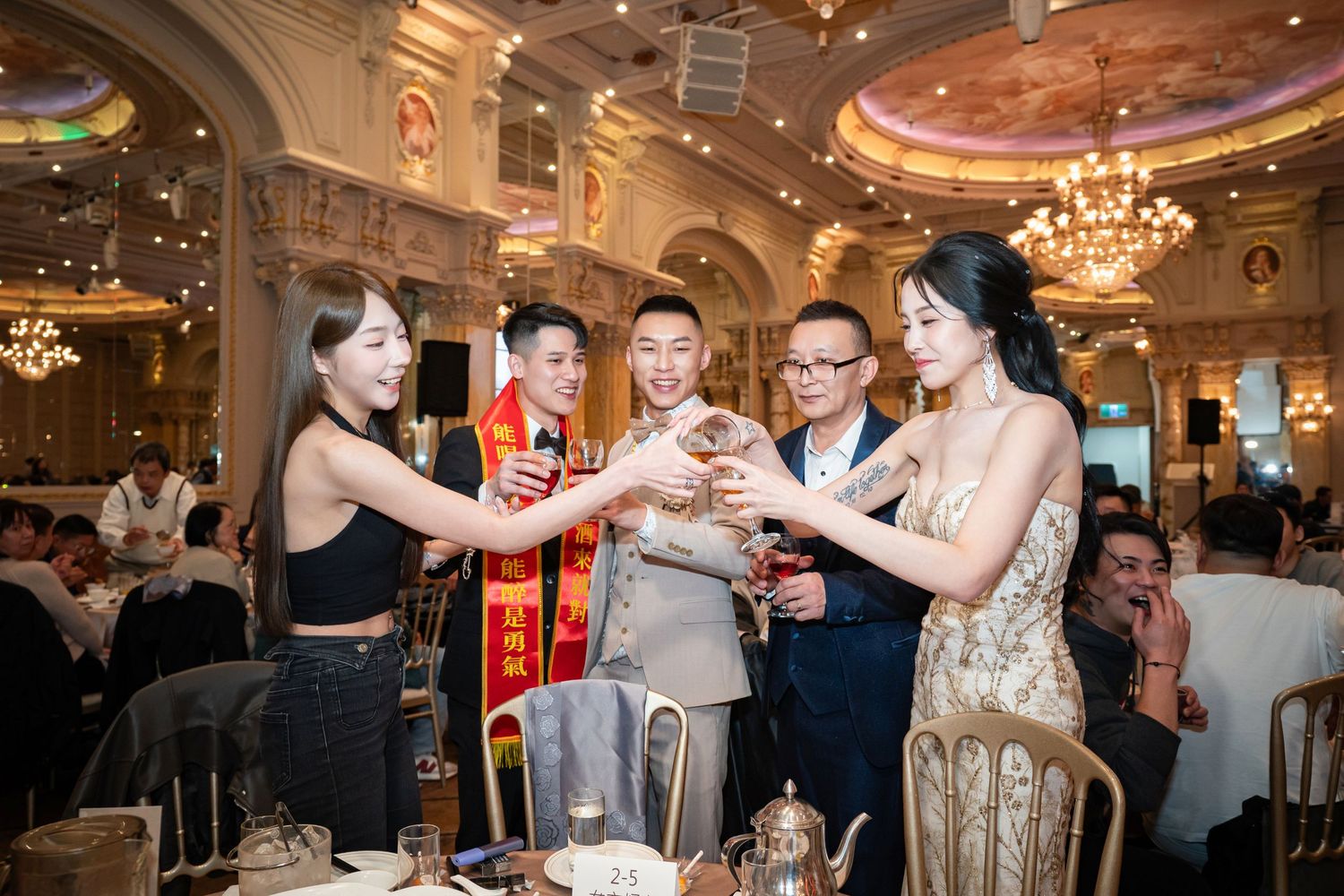 Wedding guests dance and celebrate together in an elegant ballroom with crystal chandeliers and ornate decor.