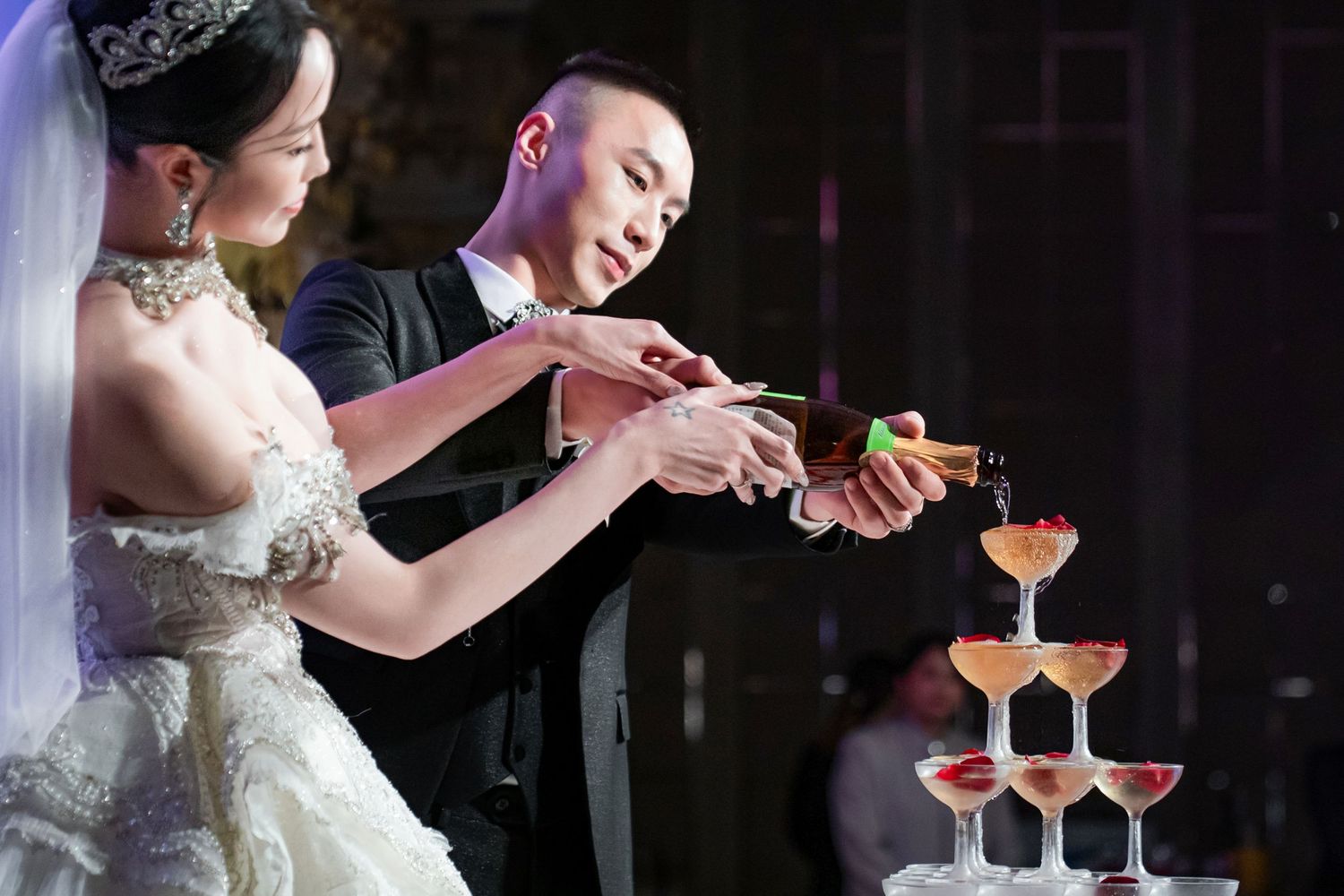 A couple pours champagne into a tower of glasses during their wedding celebration.