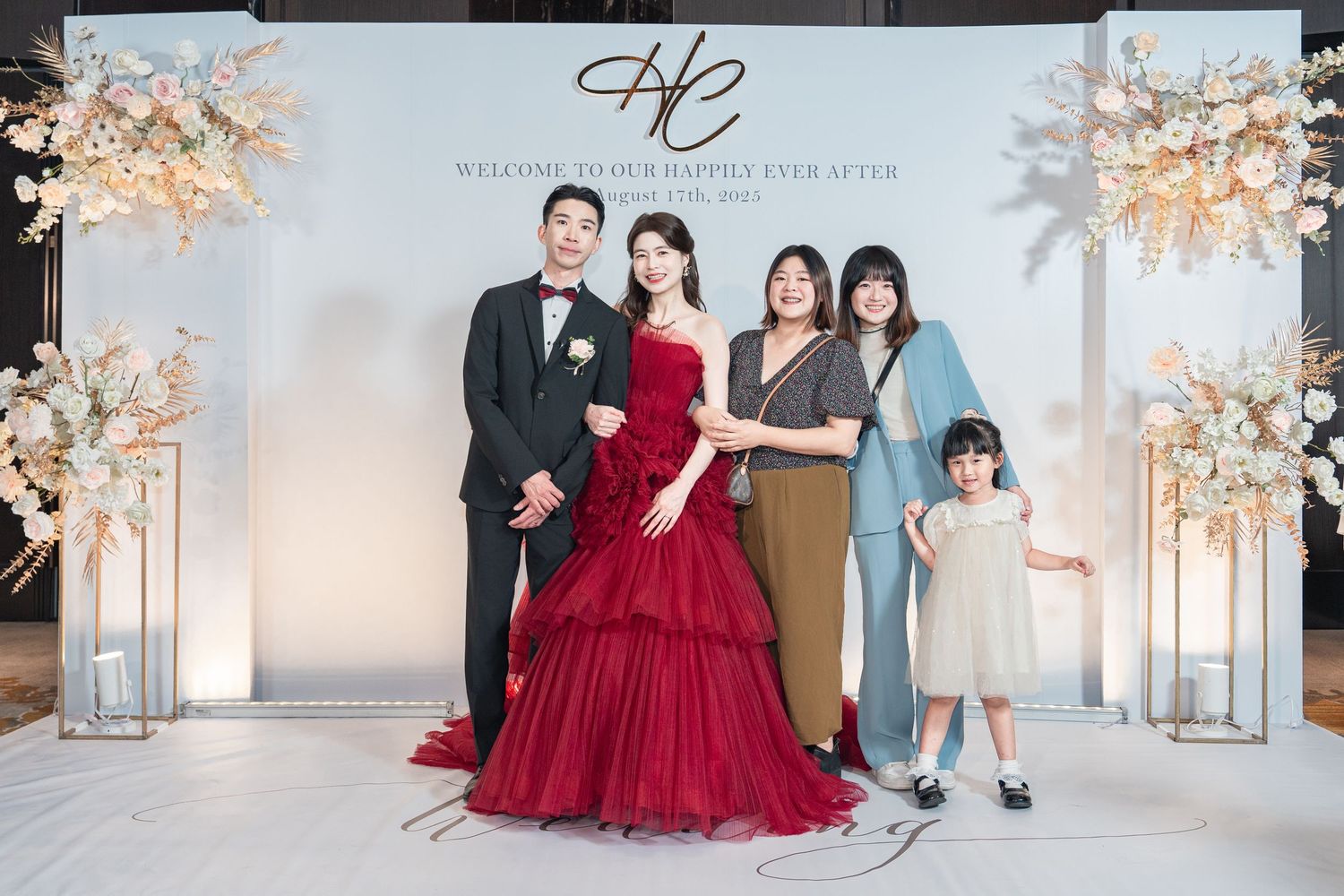 A family in coordinating formal attire poses together in an elegant white studio setting with cherry blossom decorations.