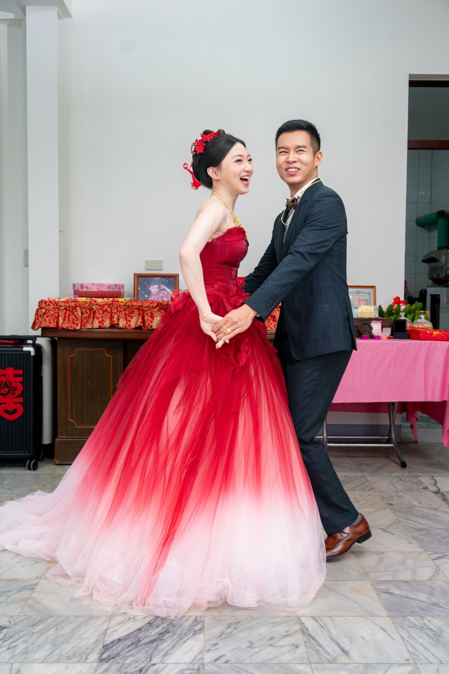 Couple dancing at wedding, bride in stunning red ombre gown, groom in black suit, smiling joyfully indoors.