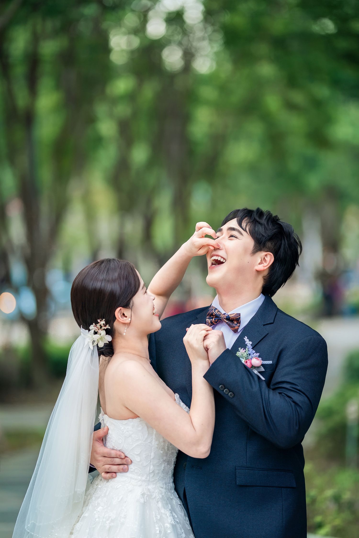 A couple shares a playful and joyful moment together in a lush green park setting during their wedding photoshoot.