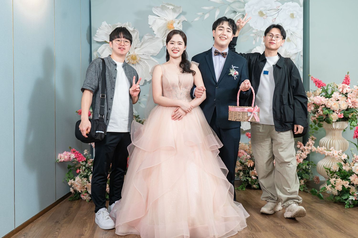 A group poses together in formal attire against a blue-gray wall with pink floral decorations.