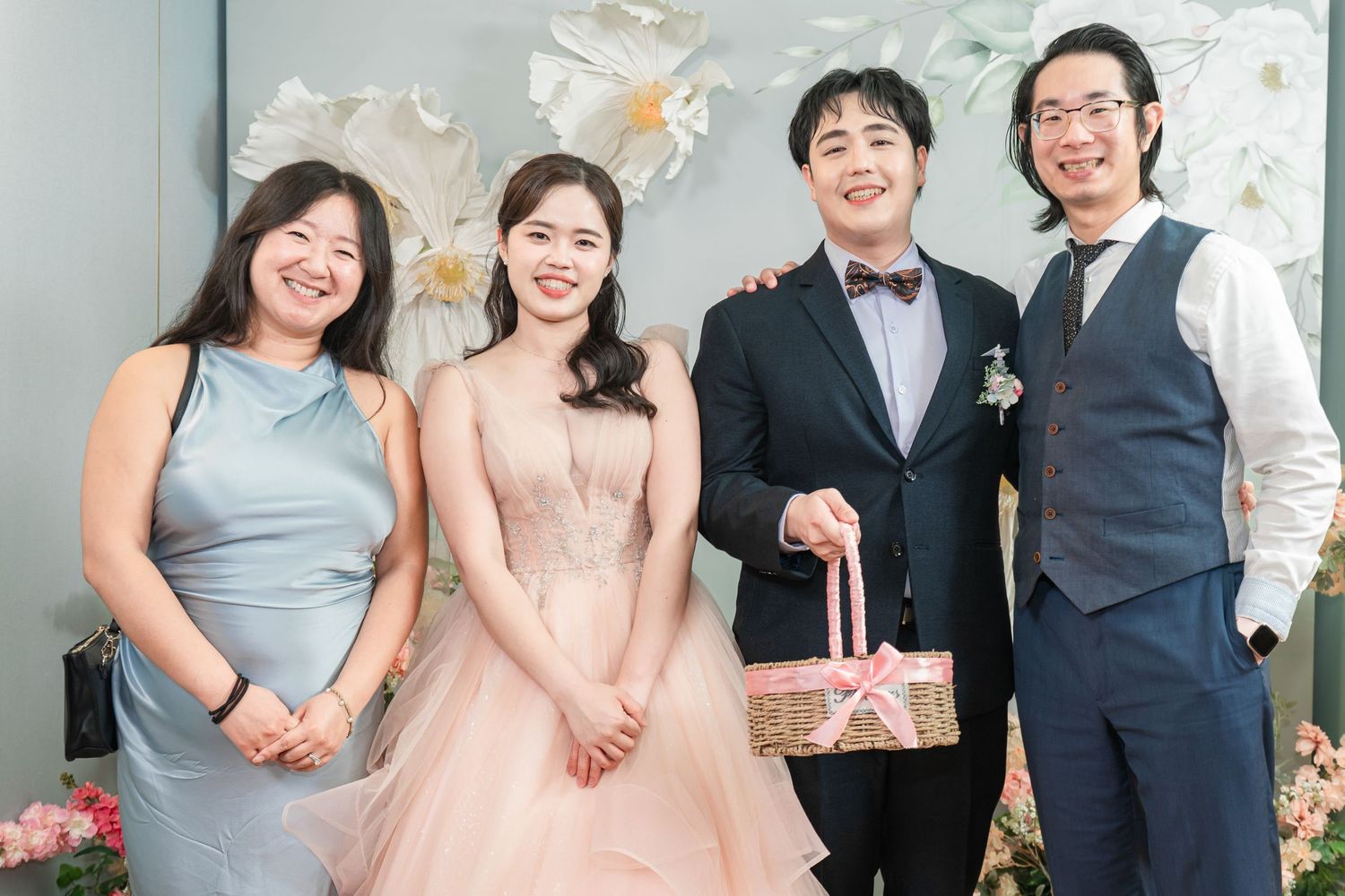 Wedding party members in formal attire pose together against a floral backdrop at an elegant celebration.