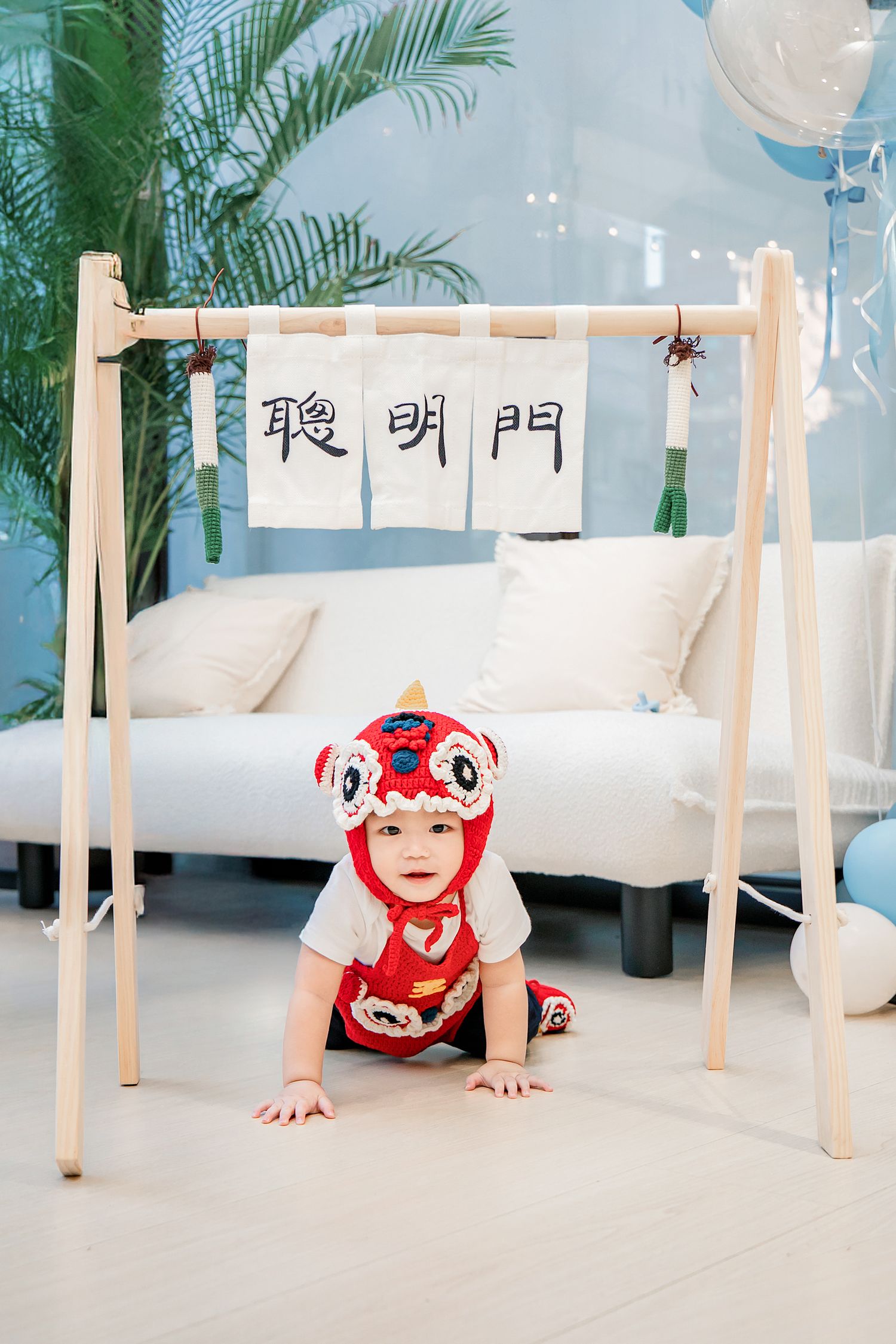 A small figure in a red outfit crawls playfully under white tables with palm plants visible in the background.