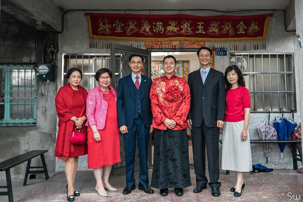 Group gathered under a red banner wearing formal attire including traditional red Chinese garments.