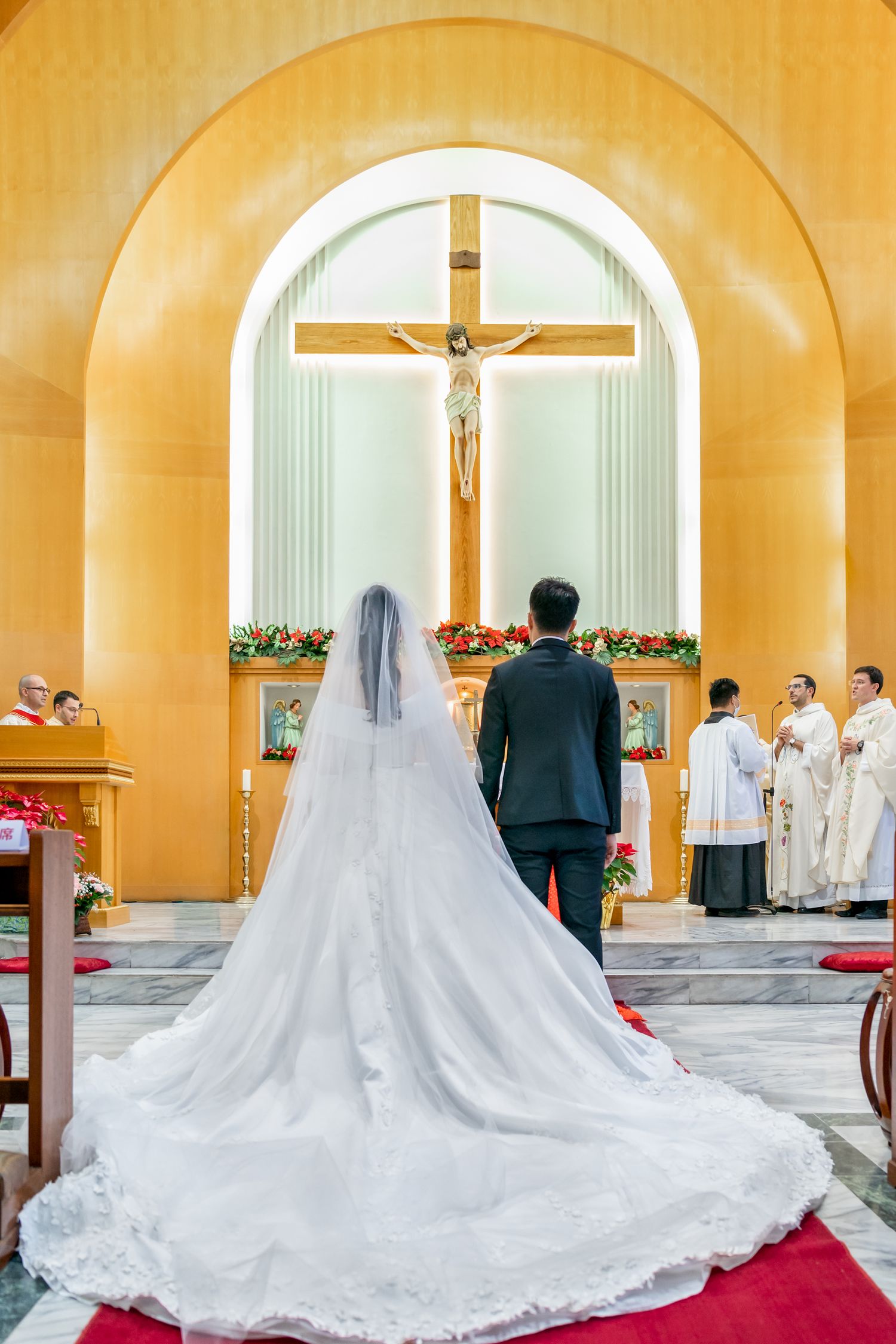 Couple stands before golden arched altar with crucifix during Catholic wedding ceremony.