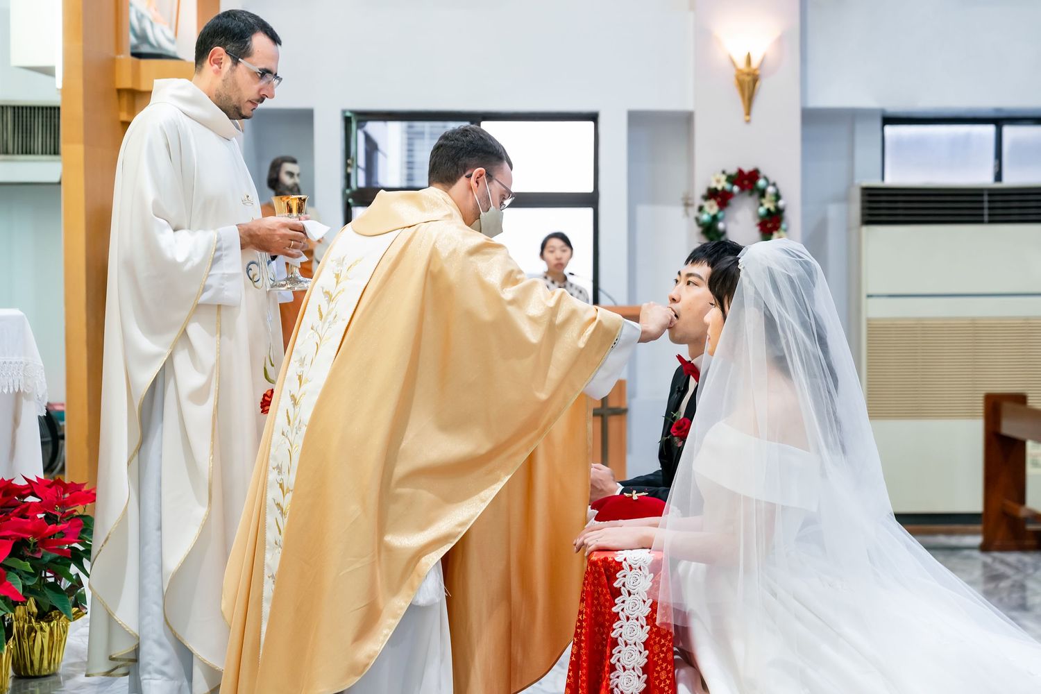 Catholic priests perform wedding ceremony blessings at altar with bride and groom during traditional mass.