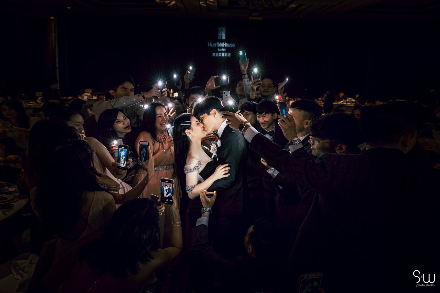Dark reception venue lit by phone lights during a wedding celebration.
