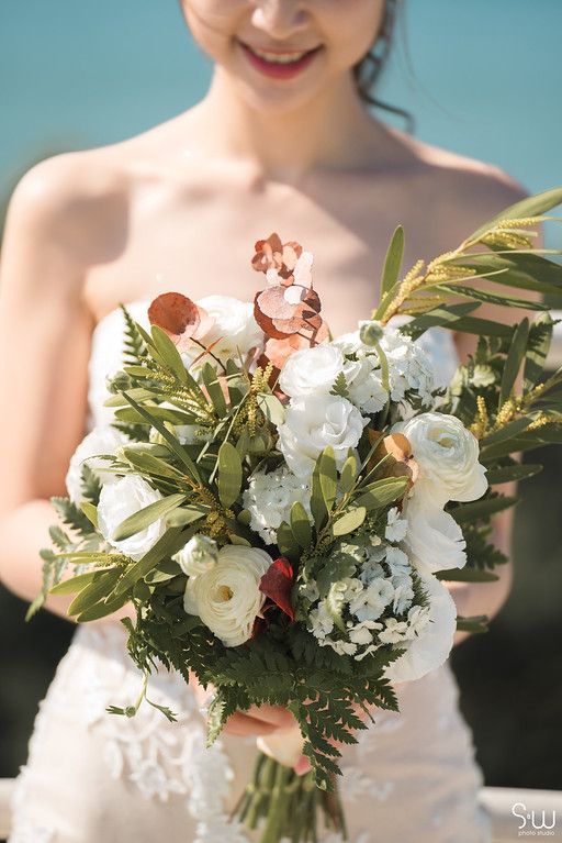 Close-up of wedding bouquet with white roses, greenery and coral accents.