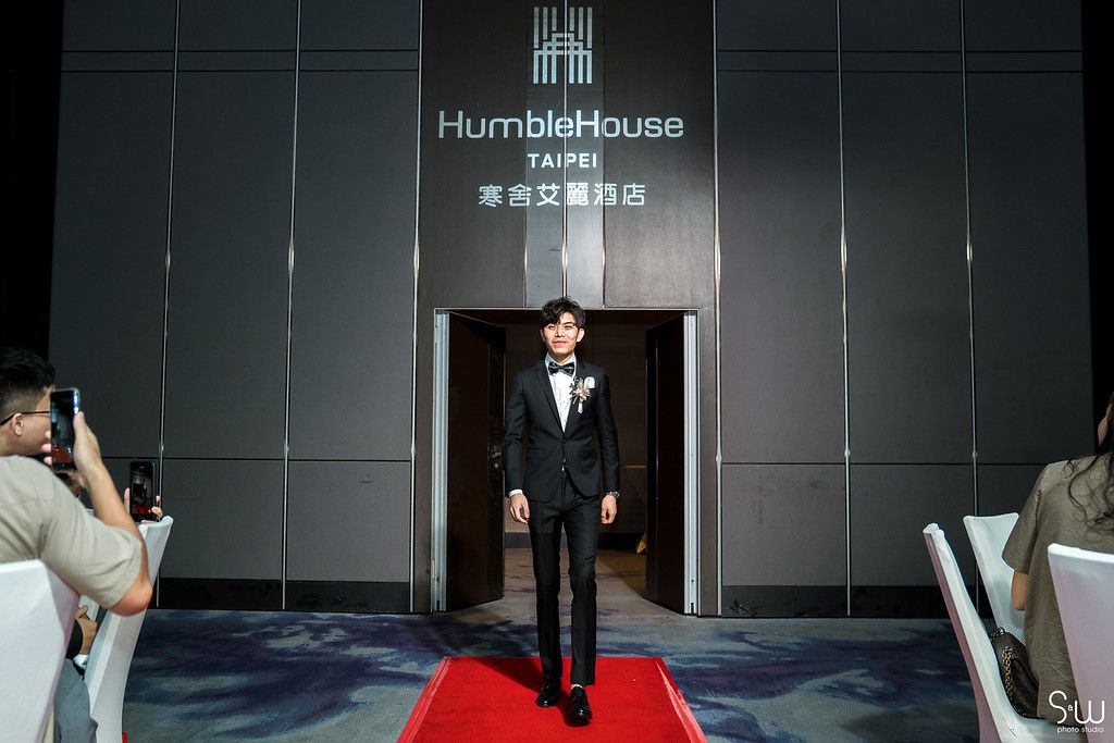 A groom walks down a red carpet at Humble House hotel entrance during a wedding ceremony.