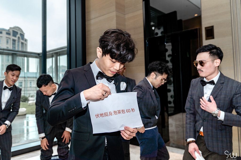 Groomsmen in formal attire reading wedding day instructions in a modern building.