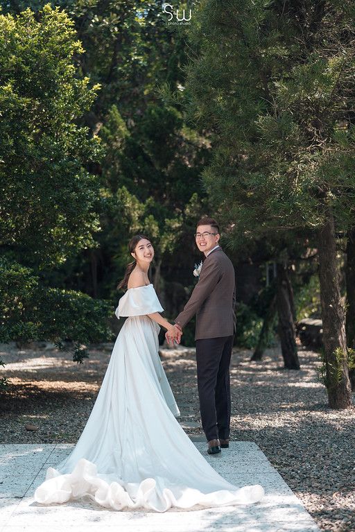 Newlyweds hold hands on garden path surrounded by lush greenery.