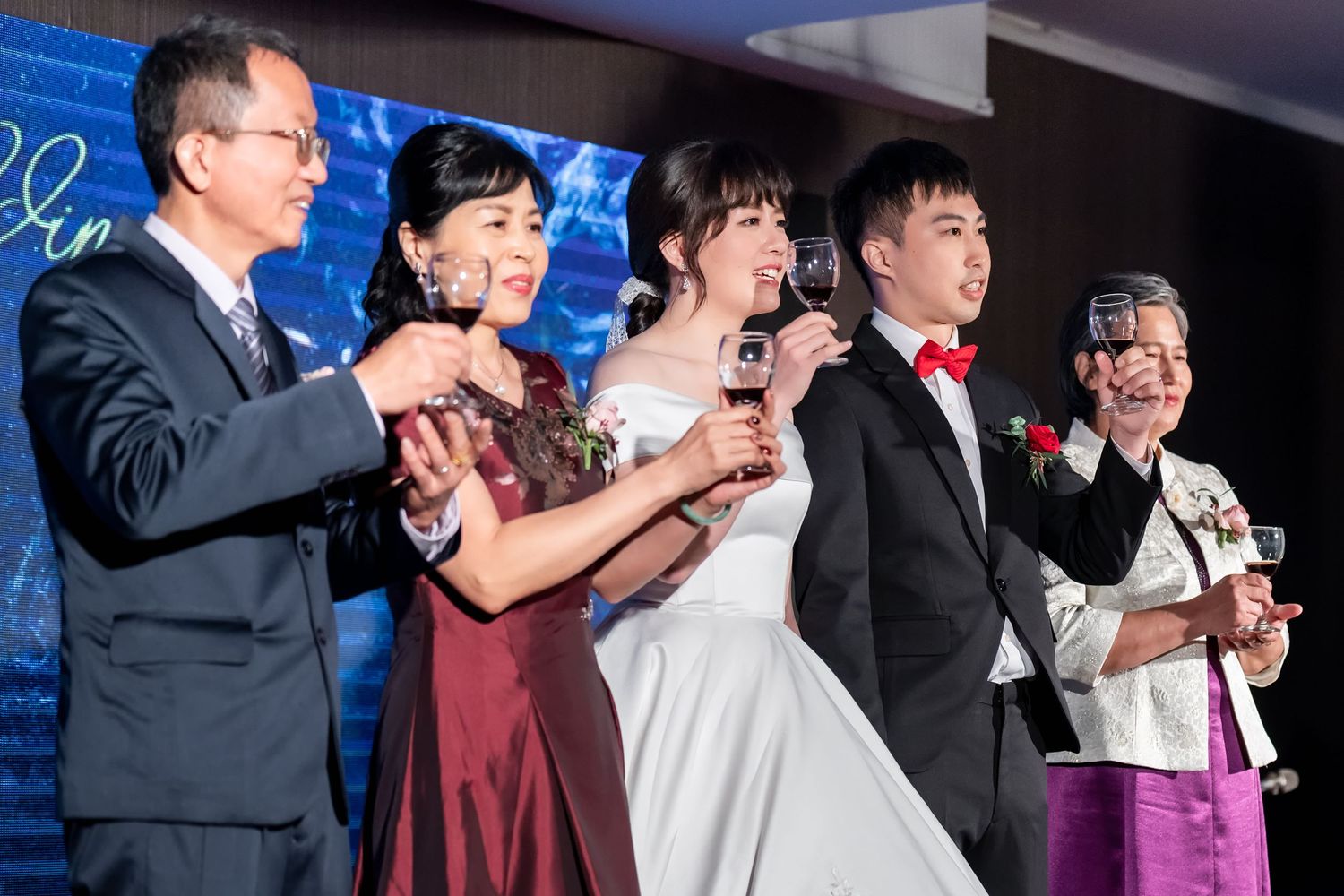 A group stands together toasting with glasses at a formal event with a blue backdrop.