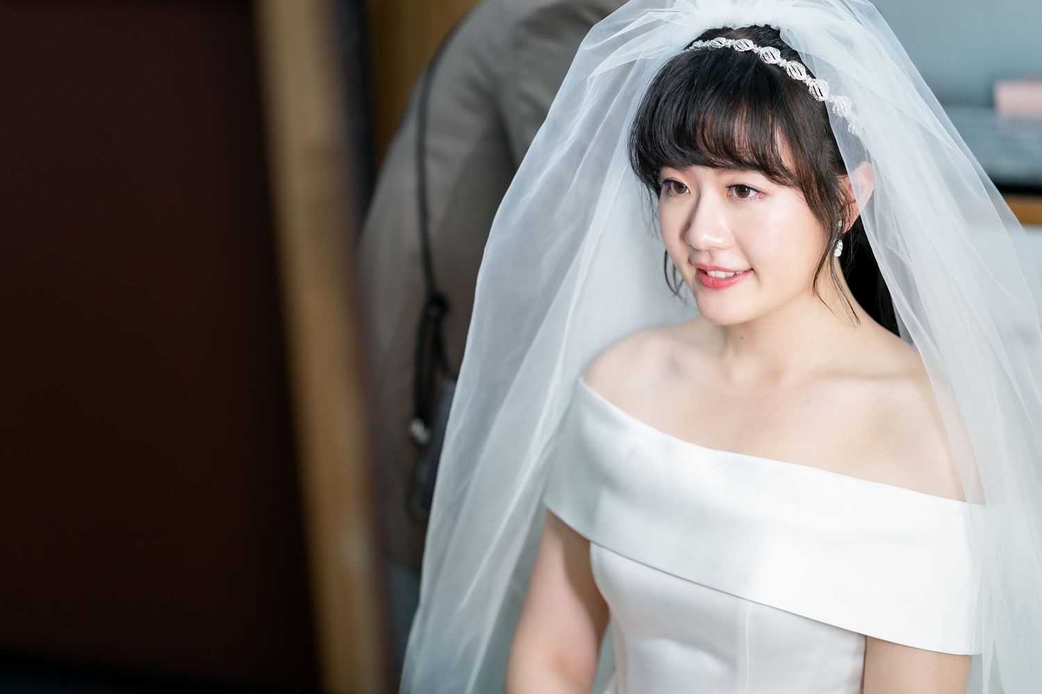 Side profile of a bride wearing an off-shoulder wedding dress and delicate veil.
