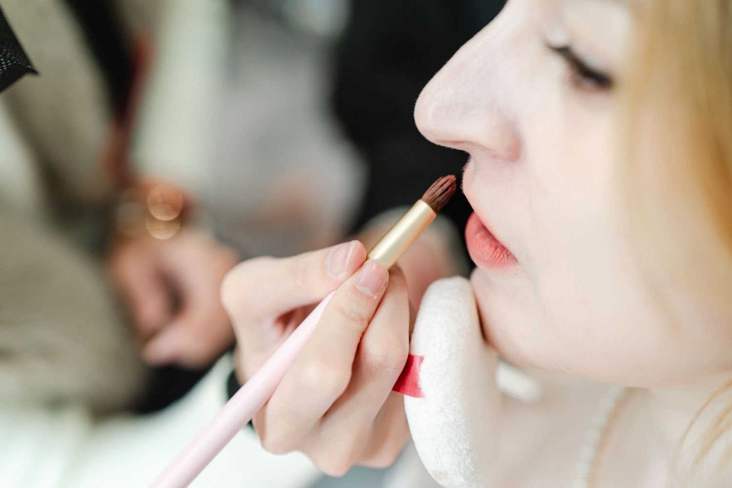 Close-up of precise lip color application during bridal makeup session.