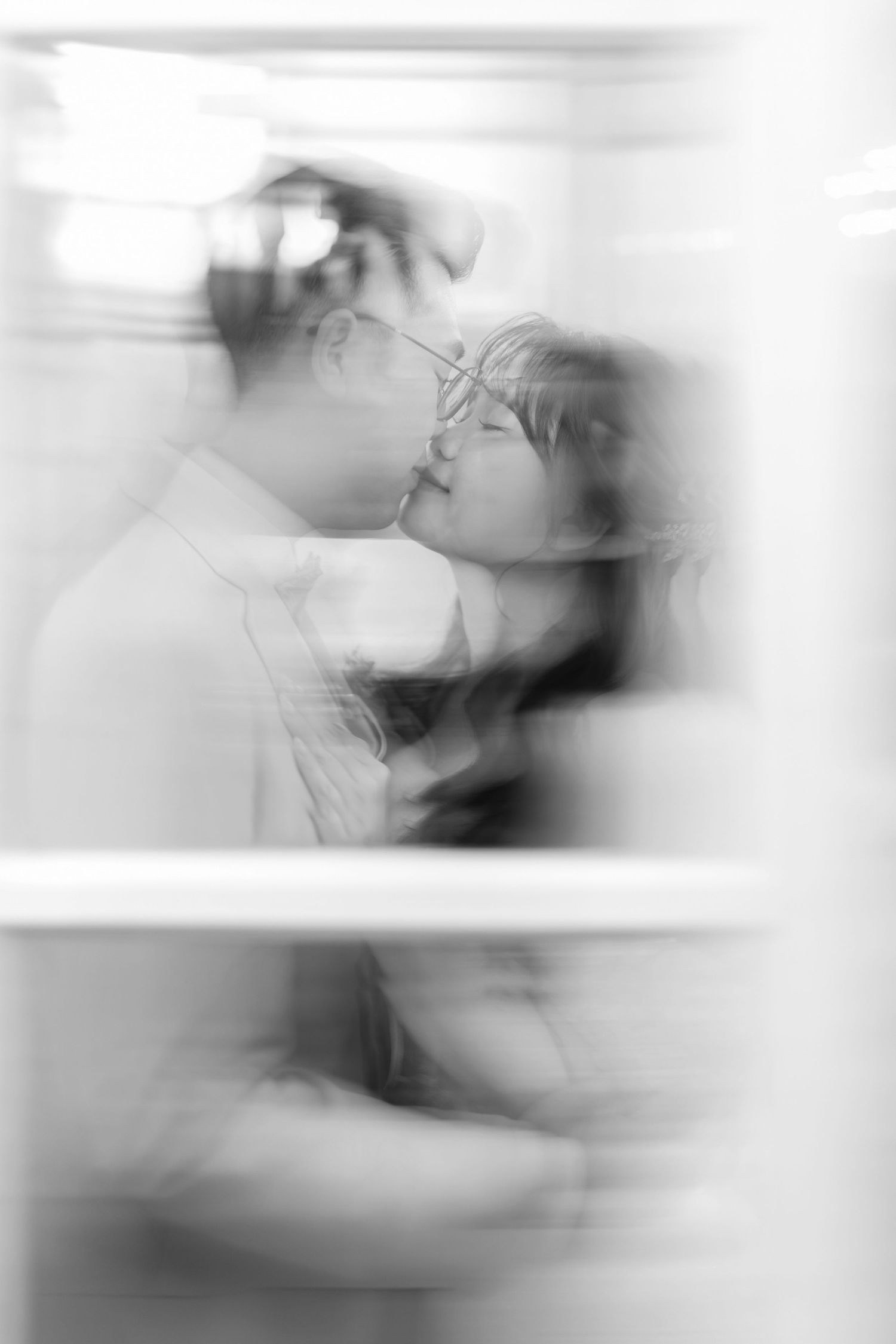 A soft, ethereal black and white photo capturing an intimate romantic moment in dreamy, blurred motion.
