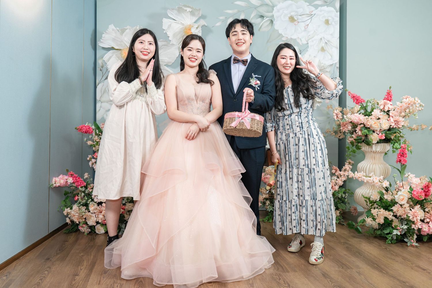 Wedding party poses together in front of floral wall decor with pink roses and white flowers.