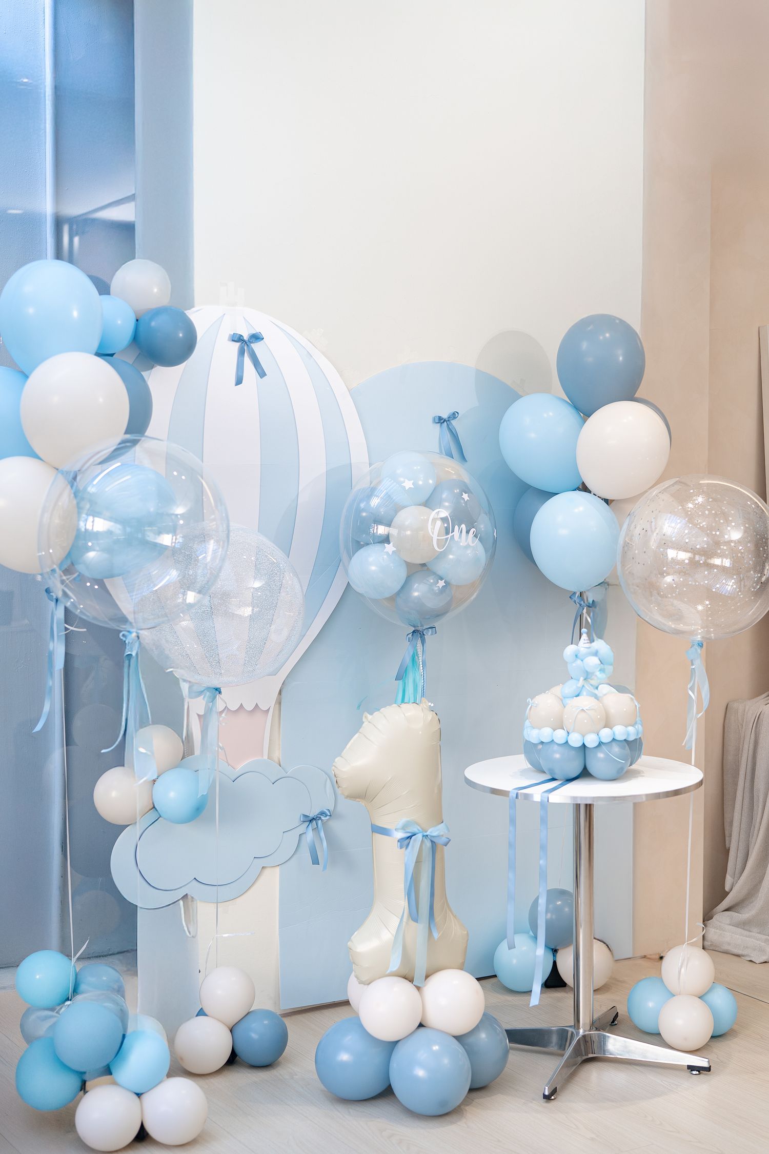 Baby shower decorations featuring an elegant blue and white balloon garland with transparent bubble balloons and cloud accents.