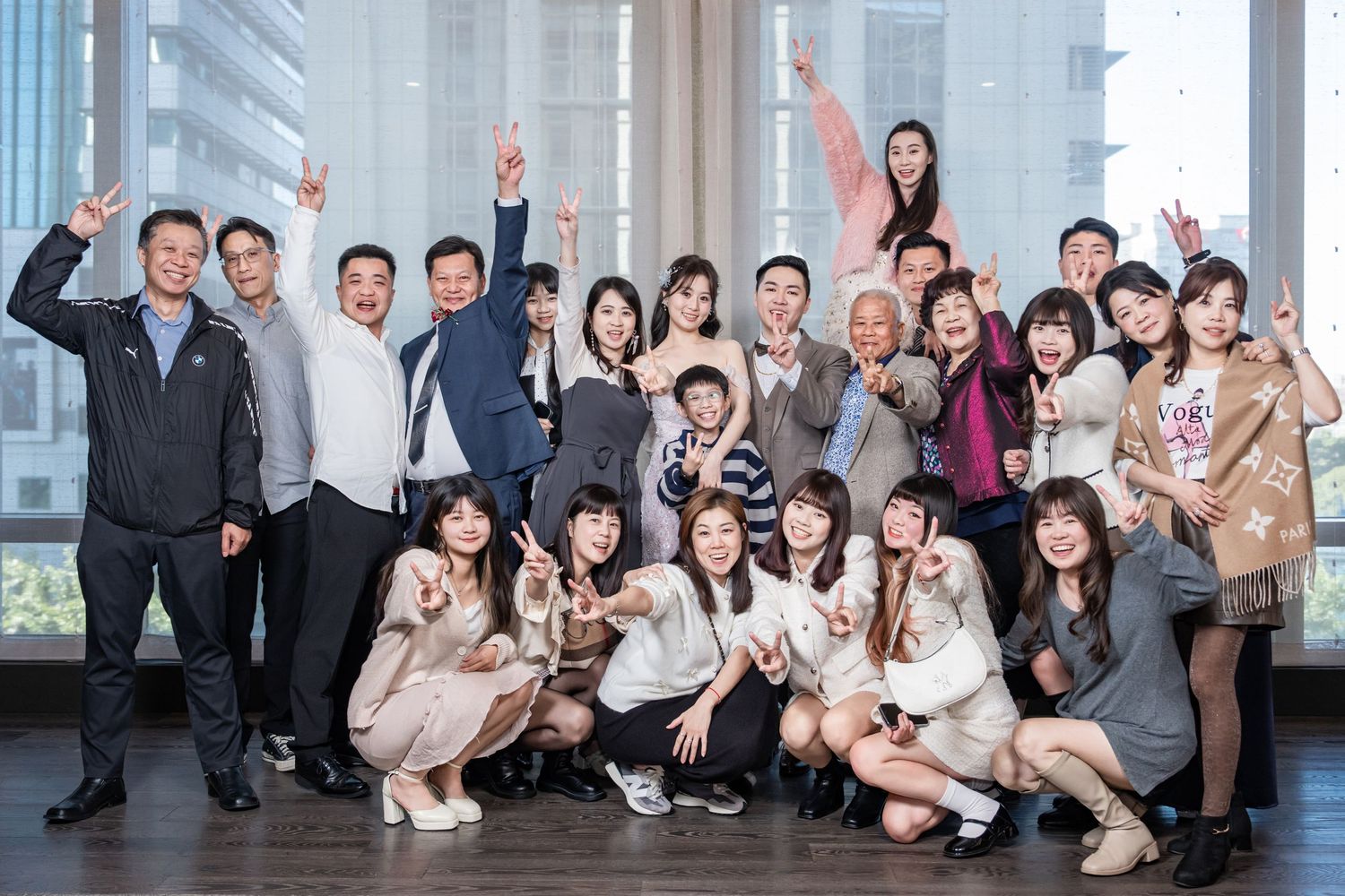 Large group of business professionals posing together in a modern office hallway with floor-to-ceiling windows.