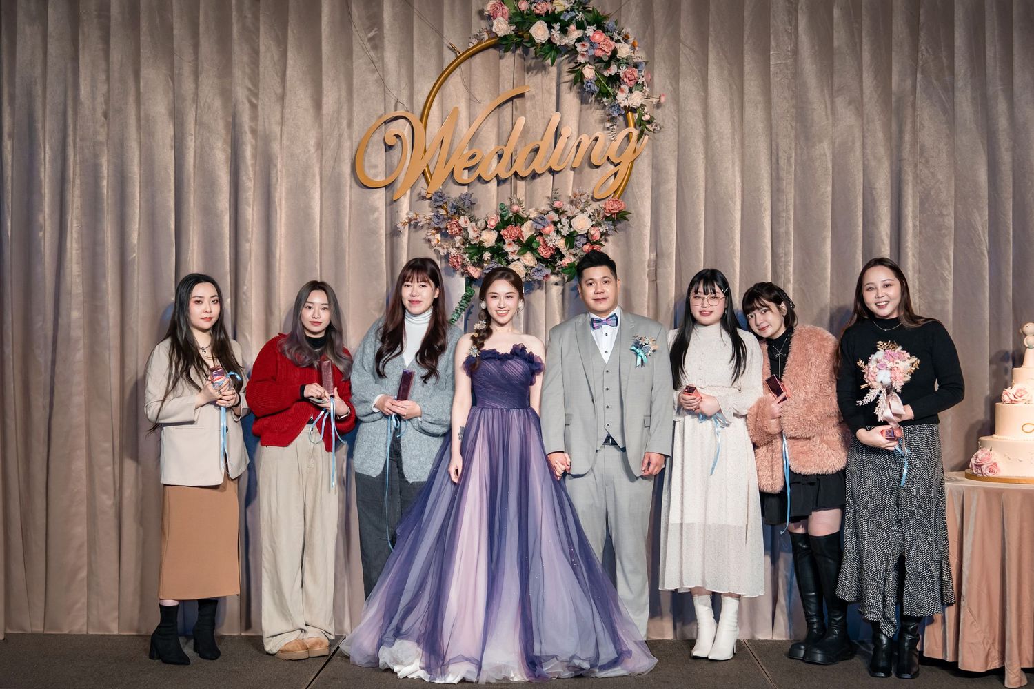 A group of people stand together at a wedding reception with a decorative backdrop featuring floral arrangements.