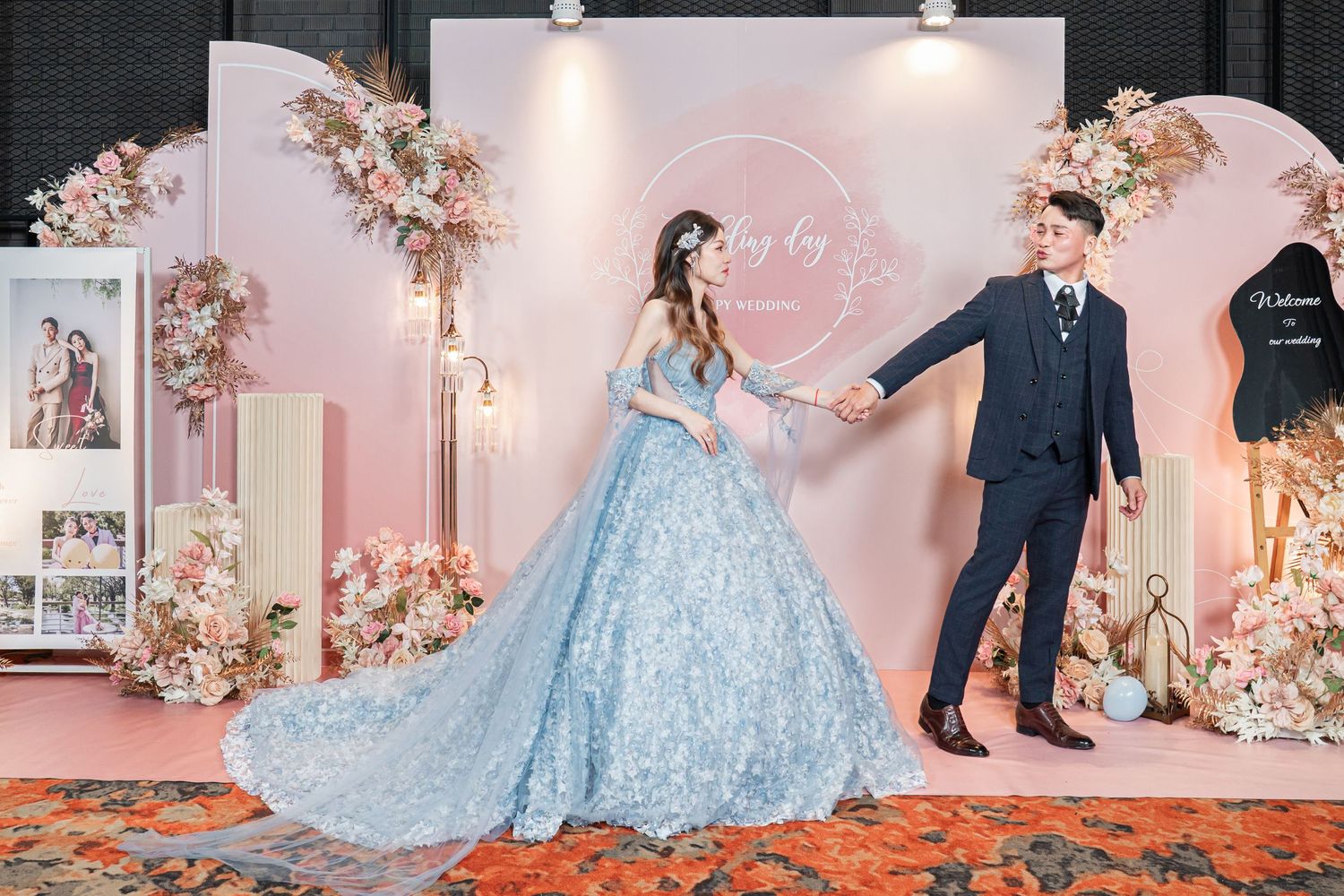 A couple in formal attire poses at an elegant wedding reception with pink floral decorations and soft lighting.