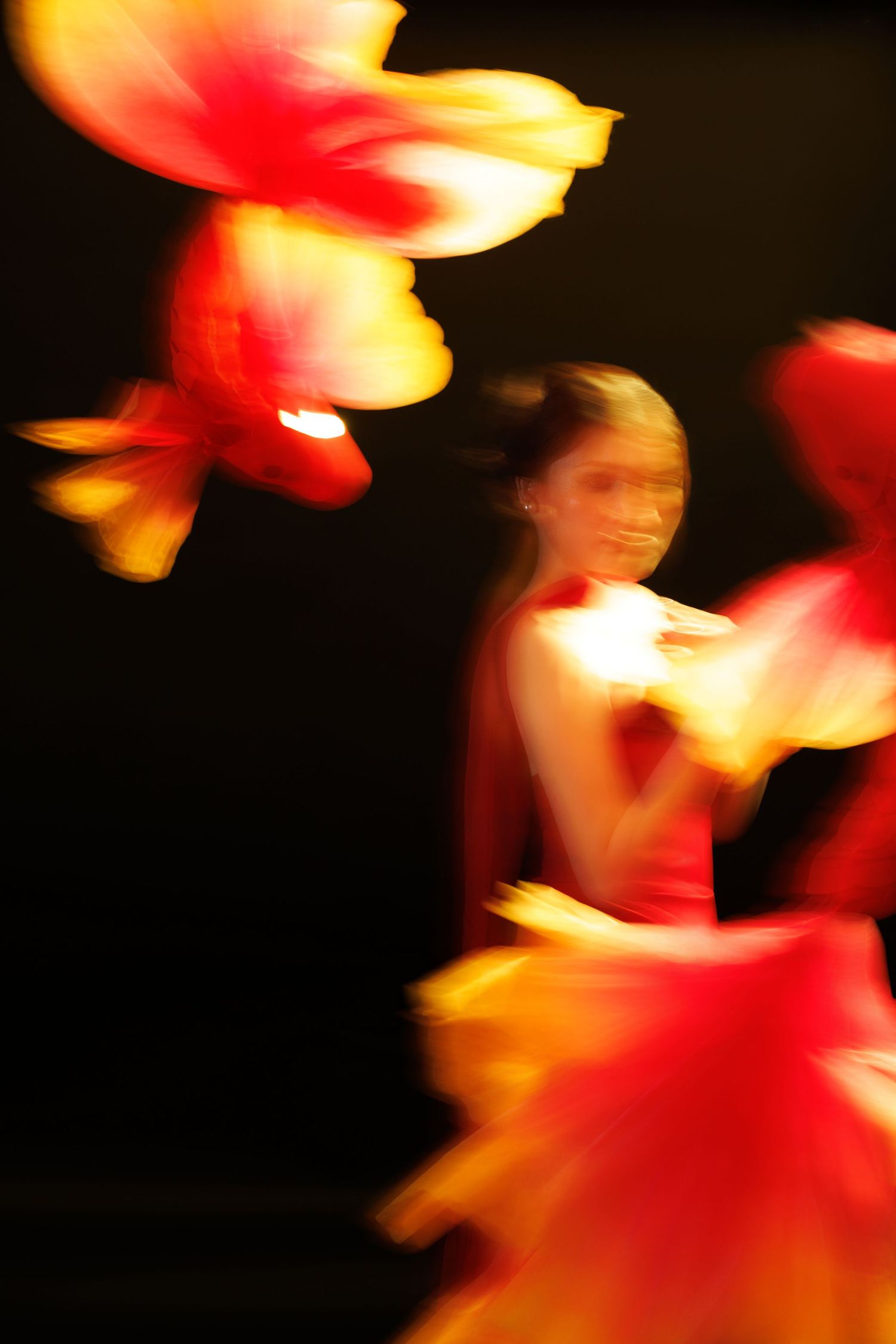 Blurred motion of a female dancer in a vibrant red and yellow costume performing an energetic dance on a dark stage.