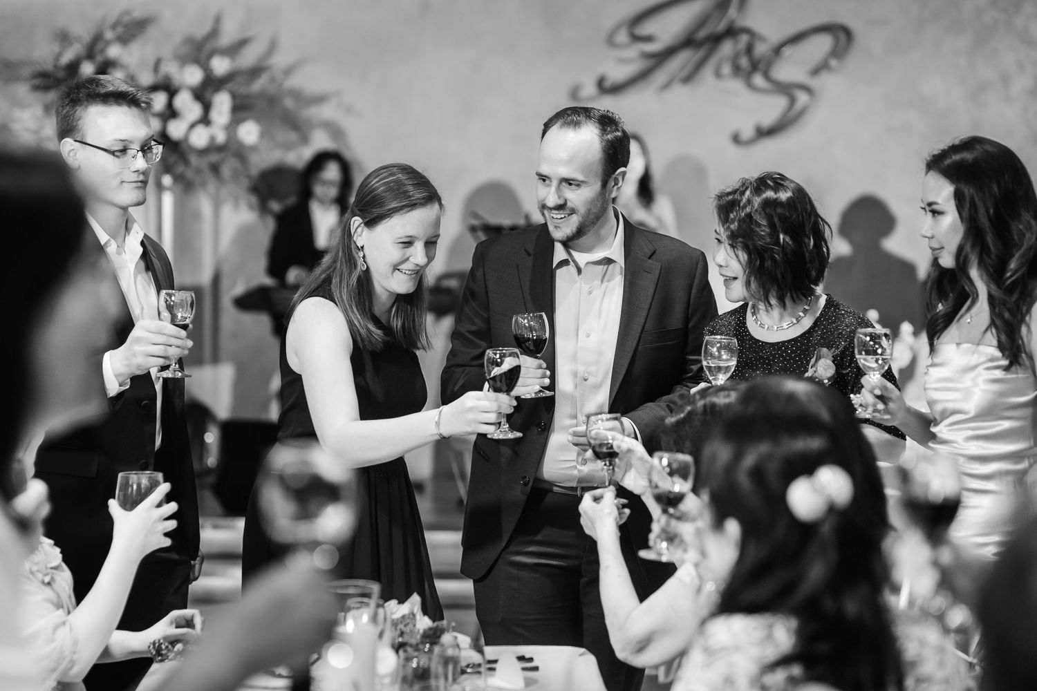 Wedding guests laugh and socialize during a lively reception gathering in black and white photography.