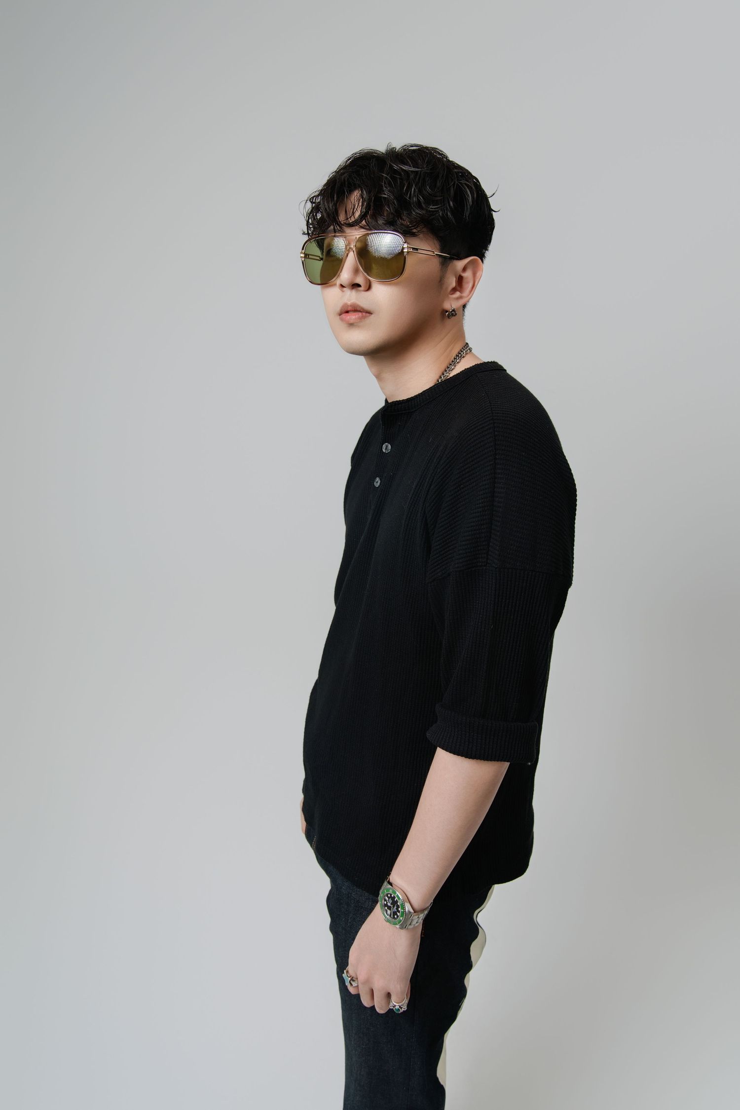 Stylish person in black shirt and sunglasses poses against gray background in minimalist fashion portrait.