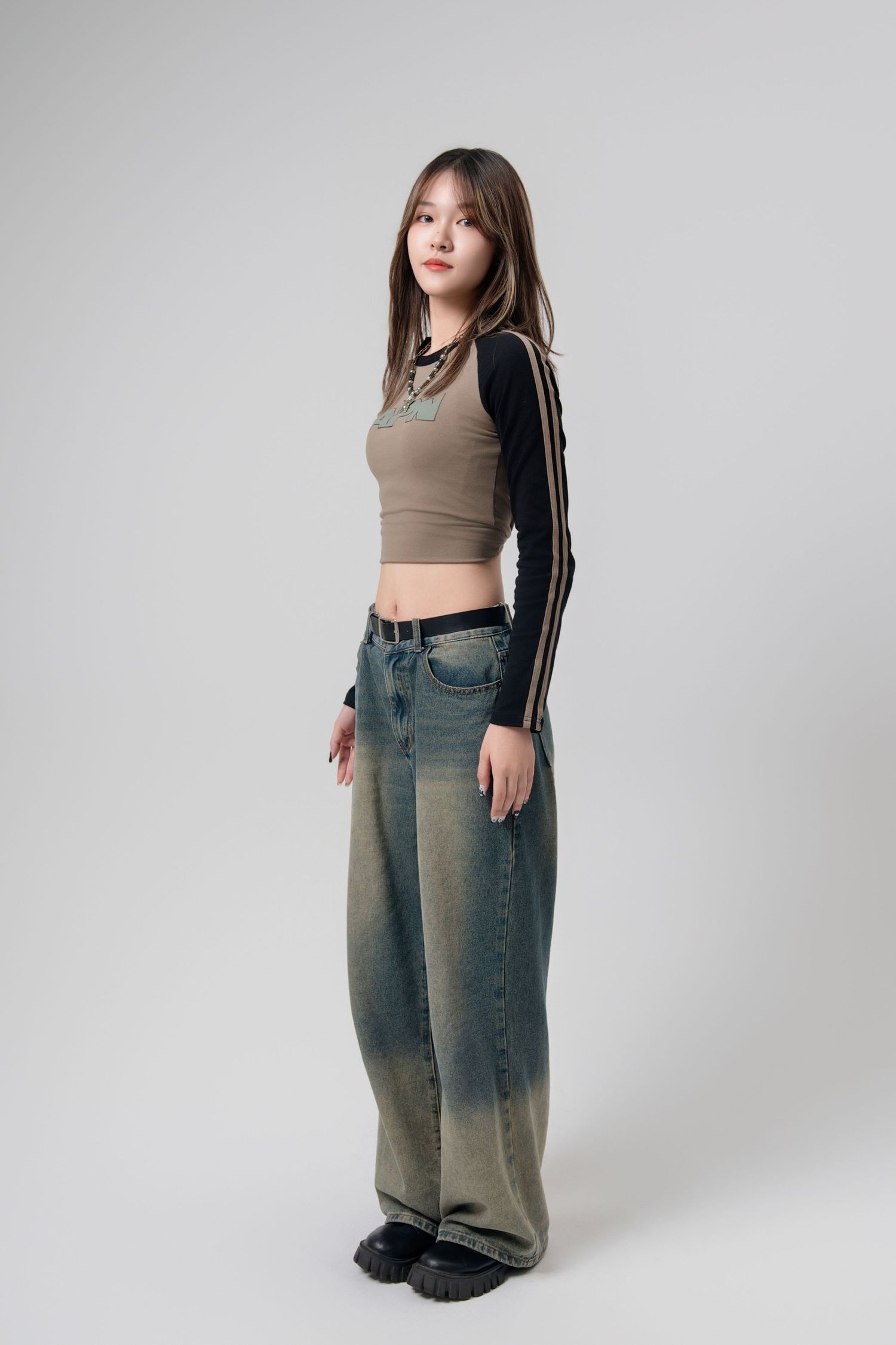 Model wearing a cropped tank top and high-waisted wide-leg jeans poses against a light gray studio background.