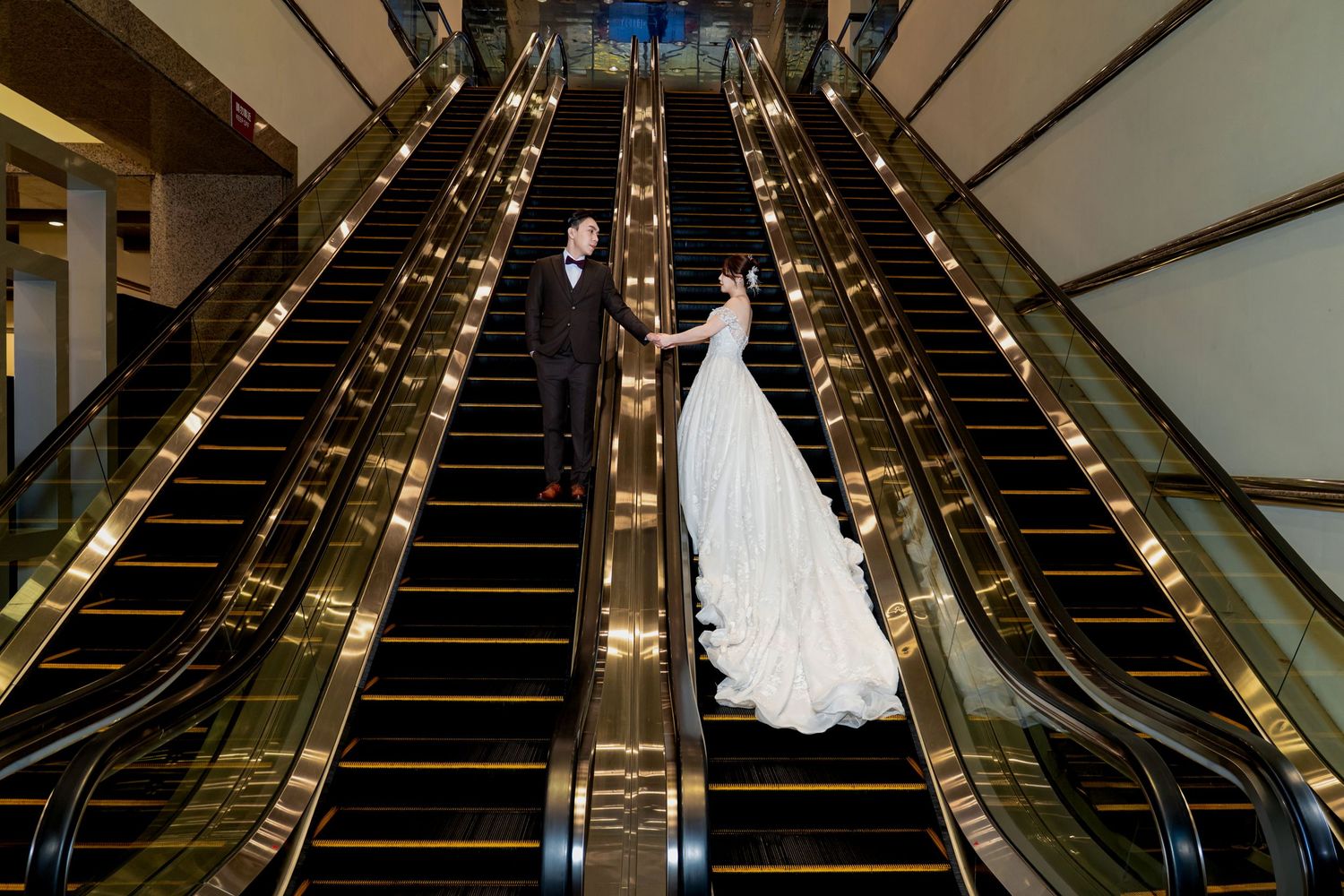 Elegant white wedding dress displayed on an escalator with gold accents and dark surroundings.