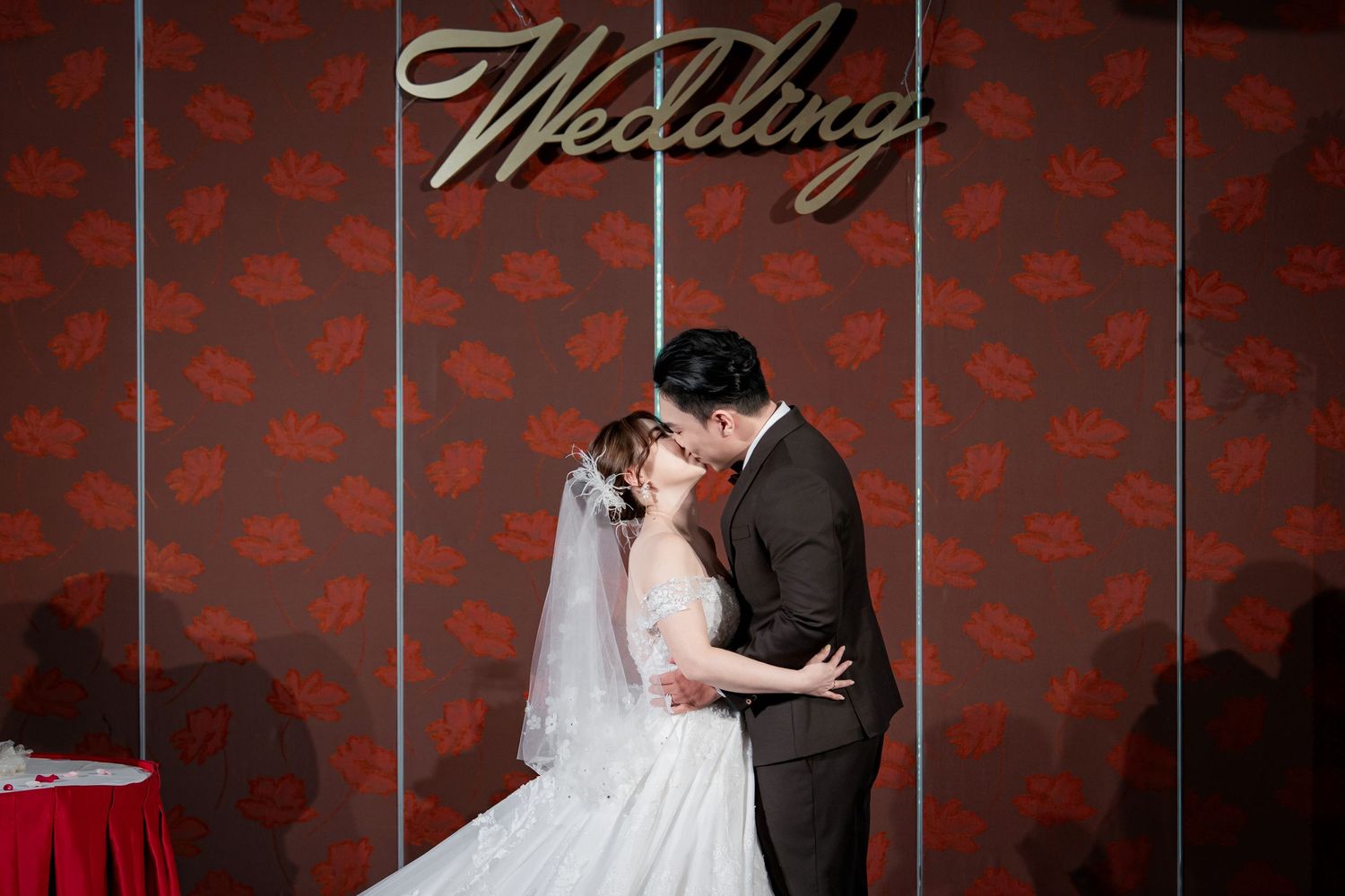 A couple shares an intimate dance moment at their wedding reception against a deep red patterned backdrop.