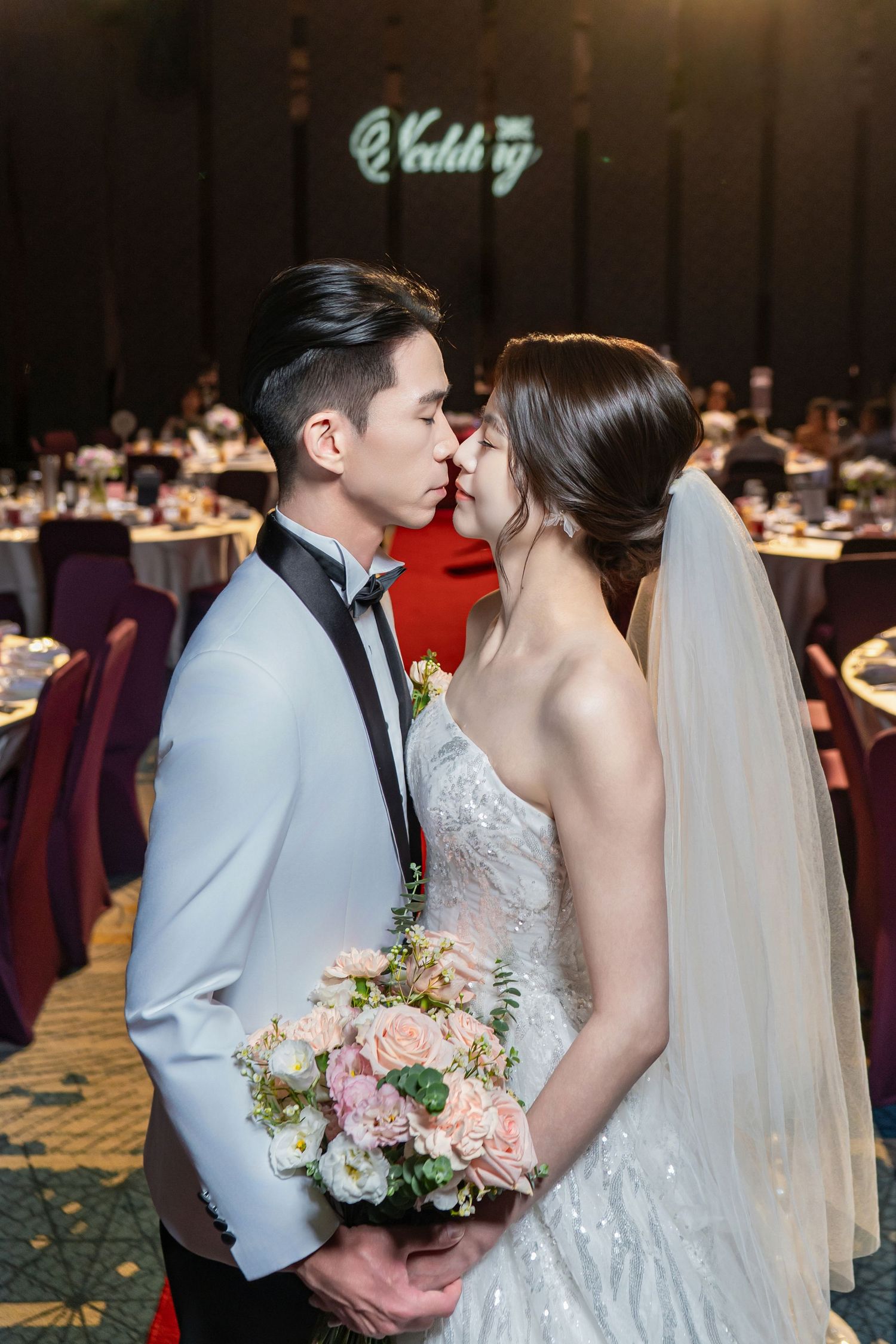 A romantic wedding moment as bride and groom share a kiss at their reception with floral bouquet and elegant decor.