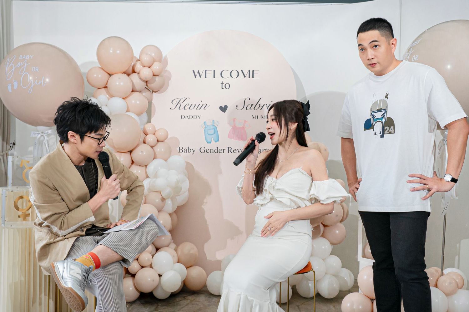 A baby shower celebration setup with balloon arch decorations in neutral beige and pink tones against a welcome sign backdrop.