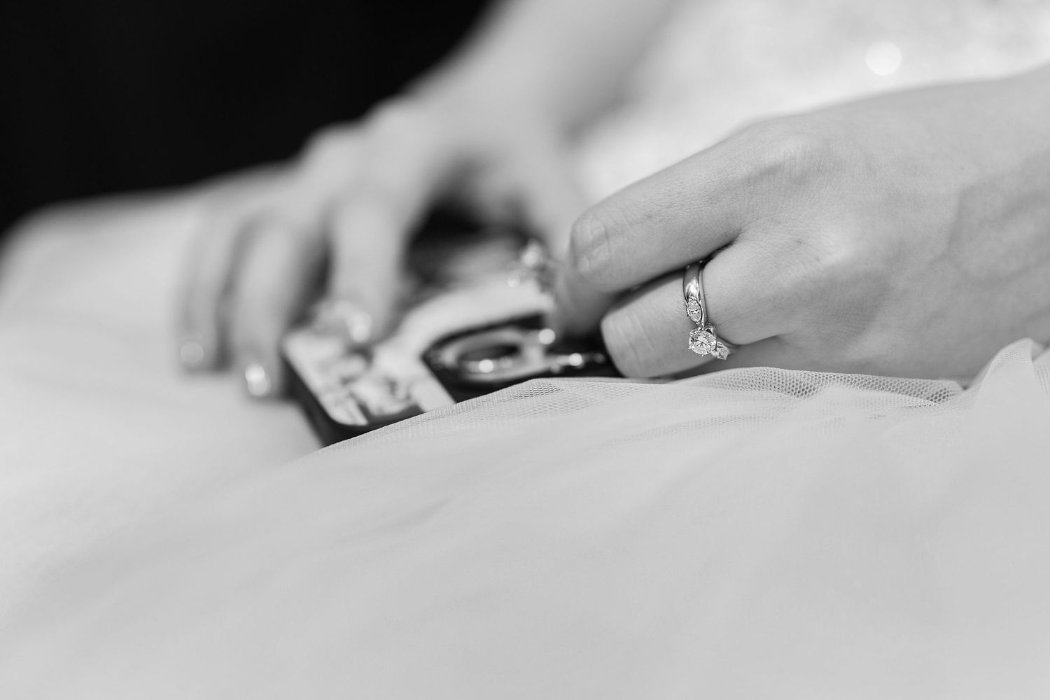 Close up black and white shot of hands wearing a ring holding vintage photographs on a white surface.