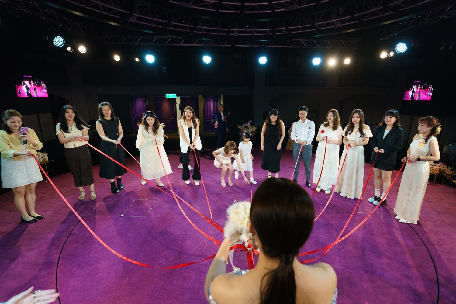 A view from behind of performers on a circular purple-lit stage during what appears to be a wedding ceremony.