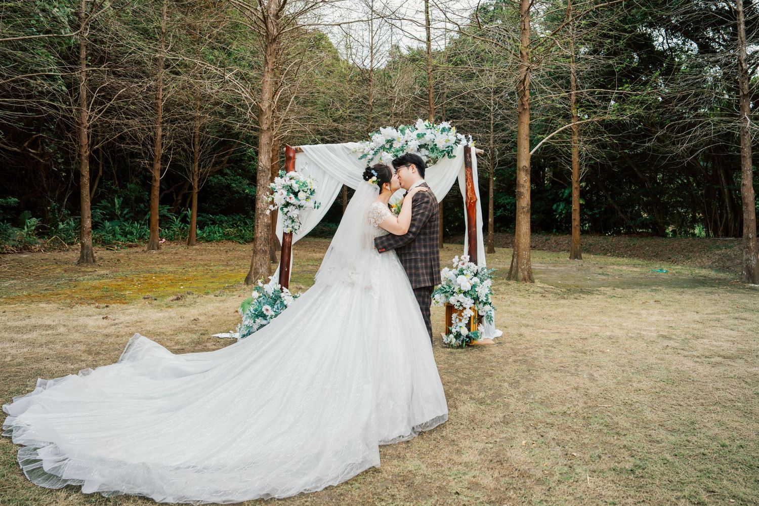 A romantic outdoor wedding scene in a wooded area with white flowing dress details and natural forest backdrop.