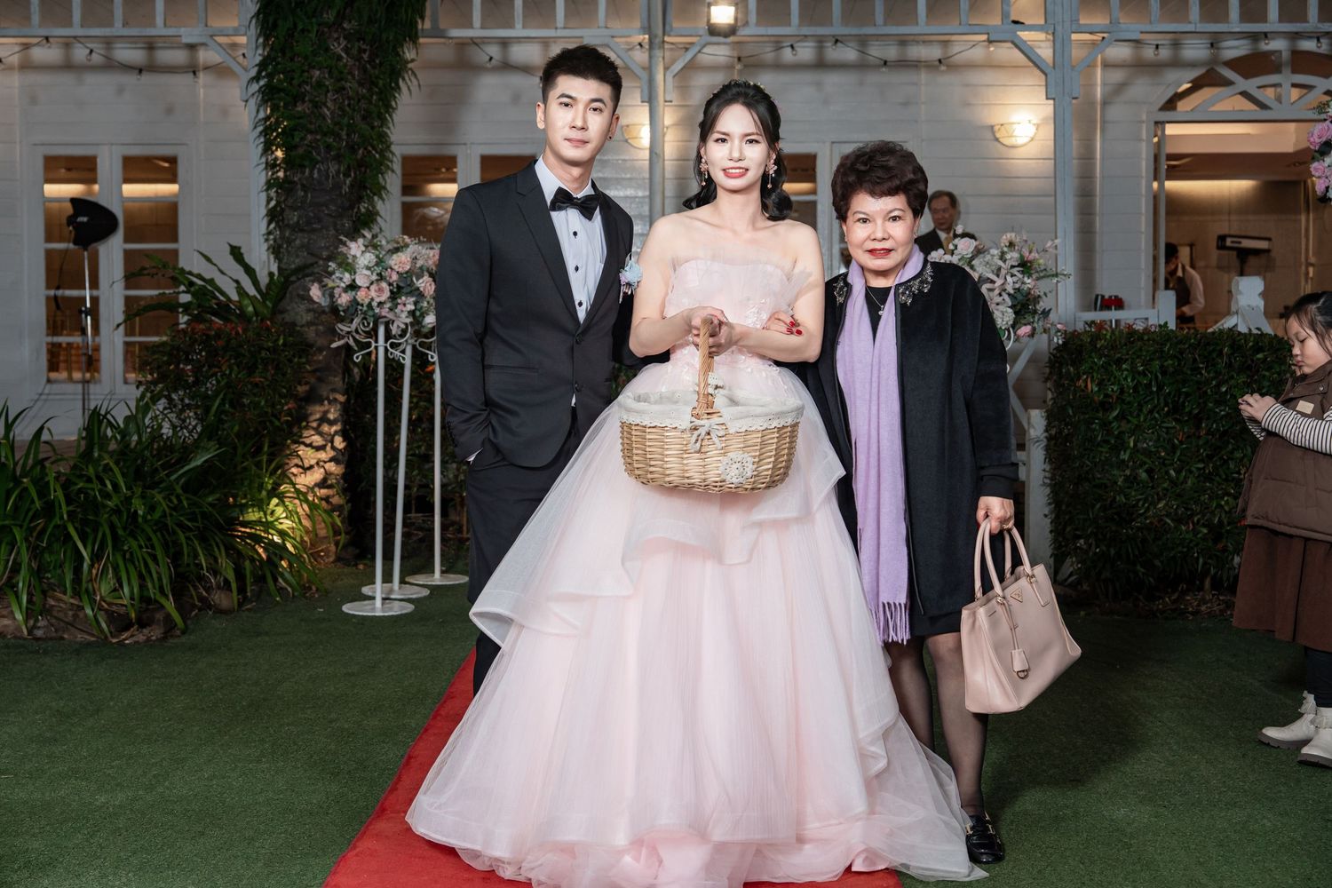 A group celebrates at an elegant wedding reception venue with decorative lighting and greenery in the background.
