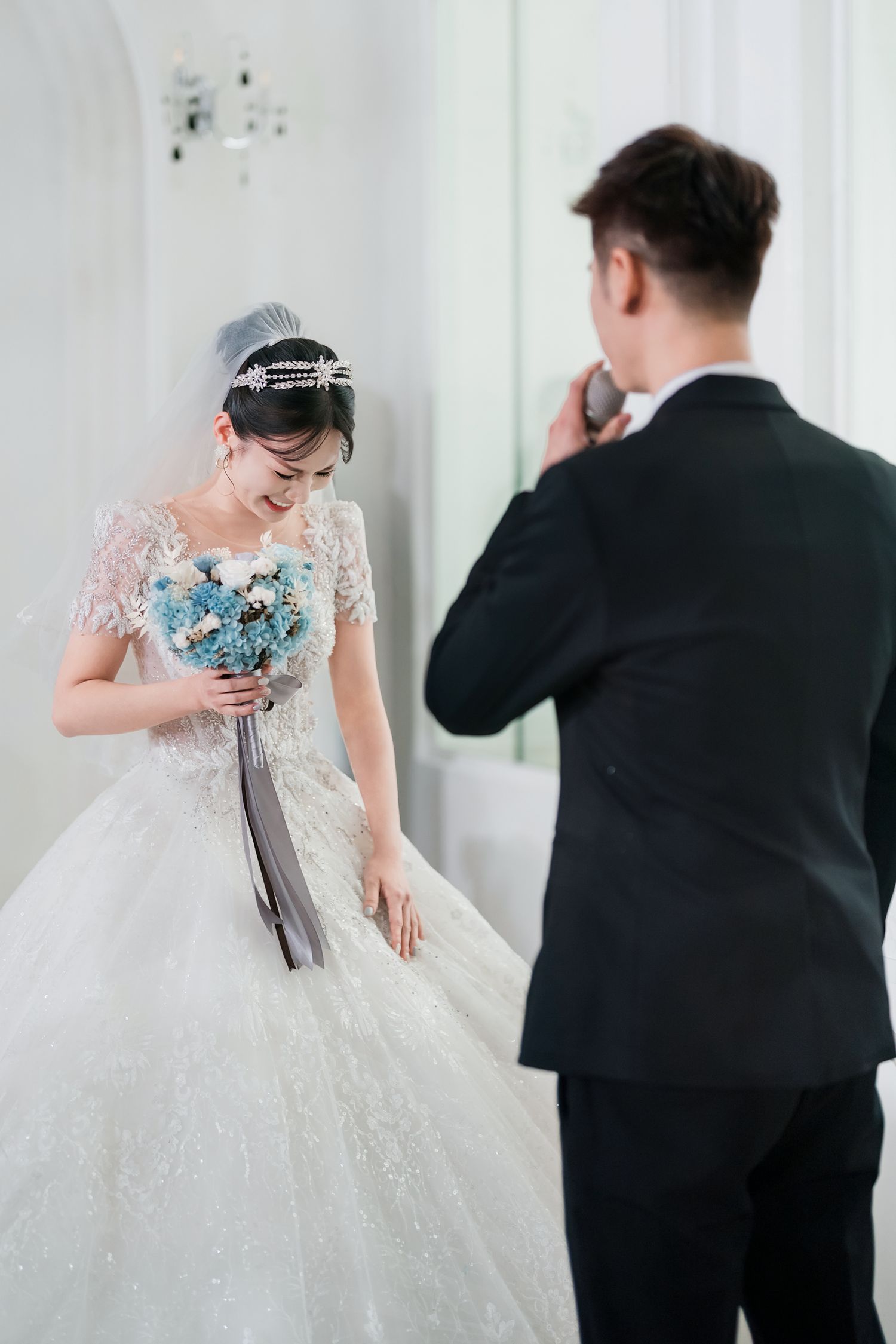 A bride in a white lace gown and groom in black suit share an emotional moment during their wedding photoshoot.