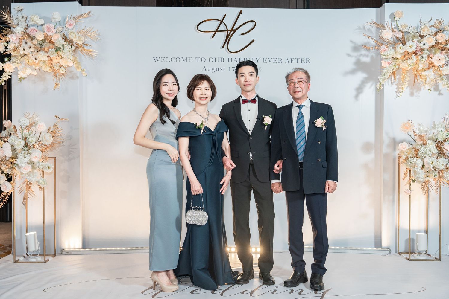 A group in elegant black and navy formalwear poses together at a formal event with decorative trees in the background.
