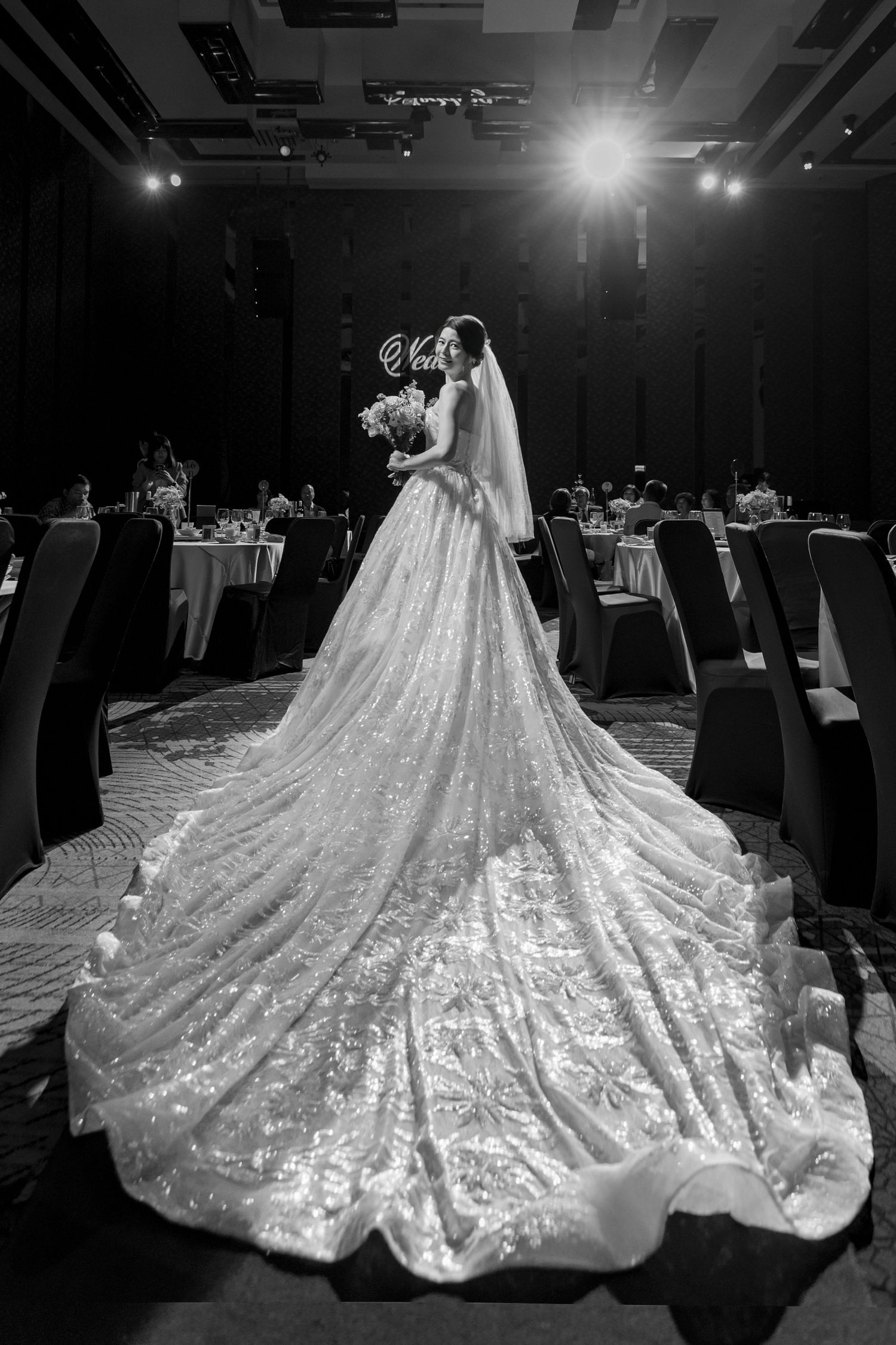 A stunning white bridal gown with an extra long sparkling train photographed at different angles on a dark ballroom floor.