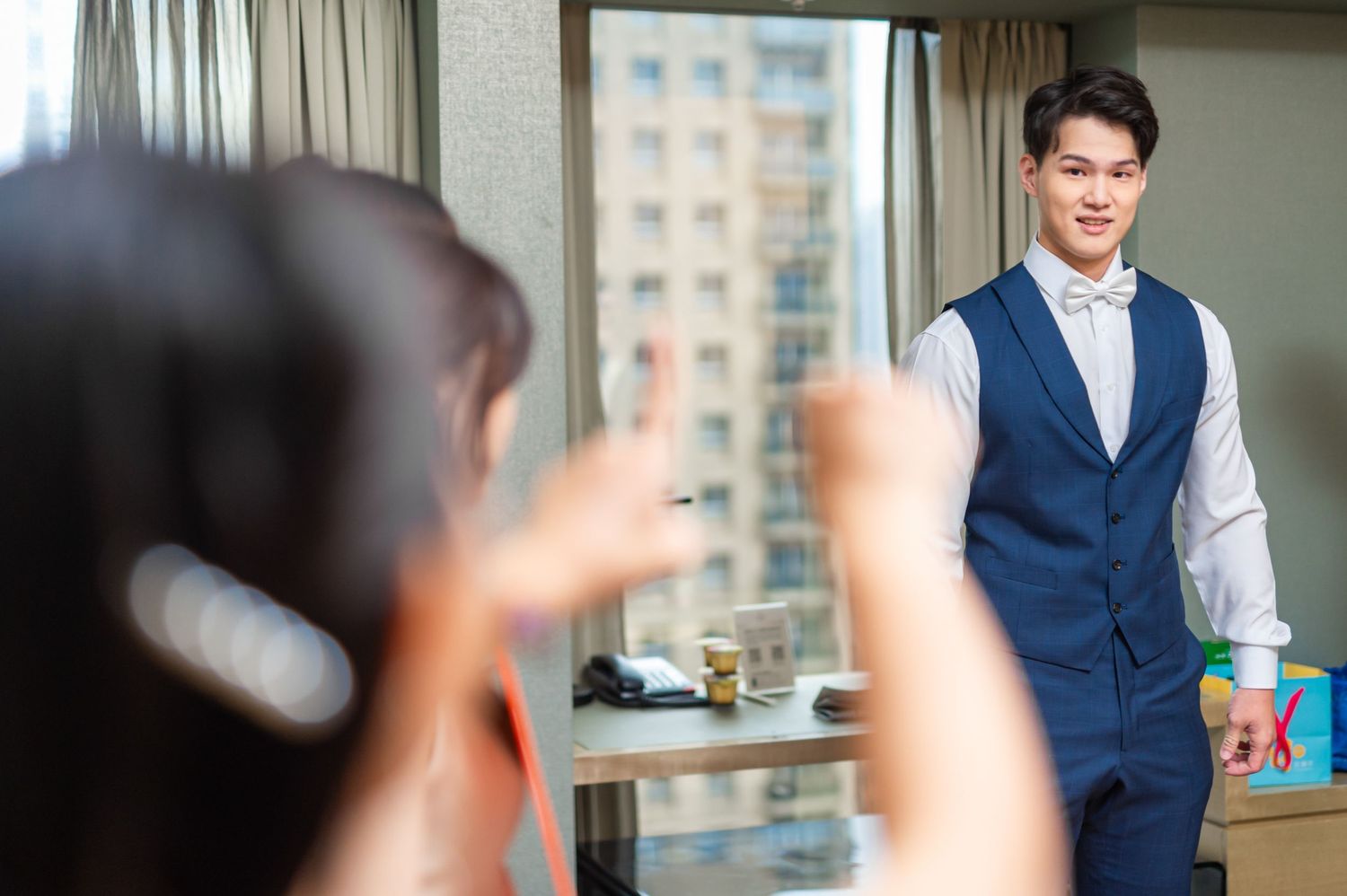 A well-dressed figure in a navy vest gets applauded by colleagues during a presentation in a bright office space.