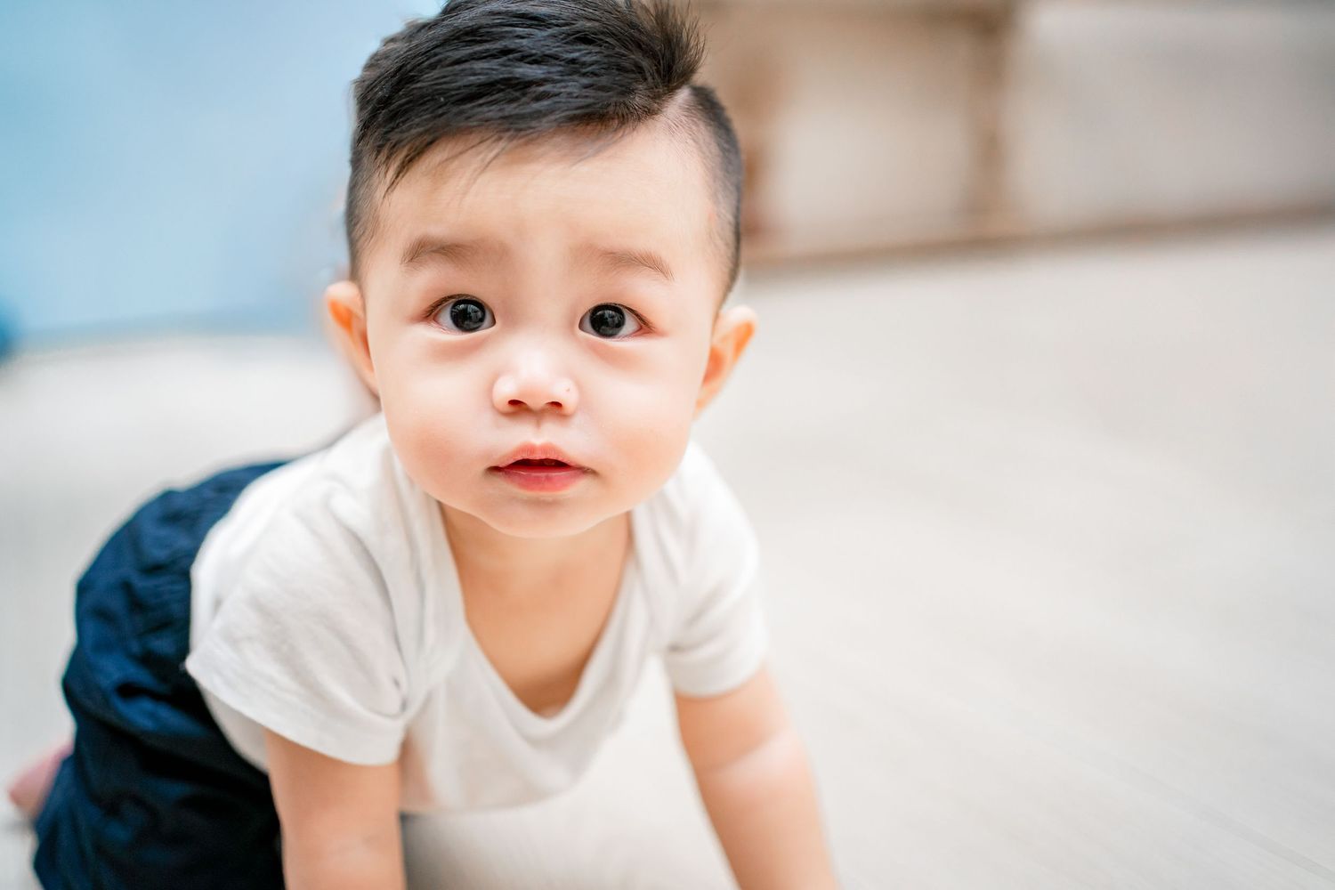 A baby in a white t-shirt crawls and plays on a light colored floor in a series of candid shots.