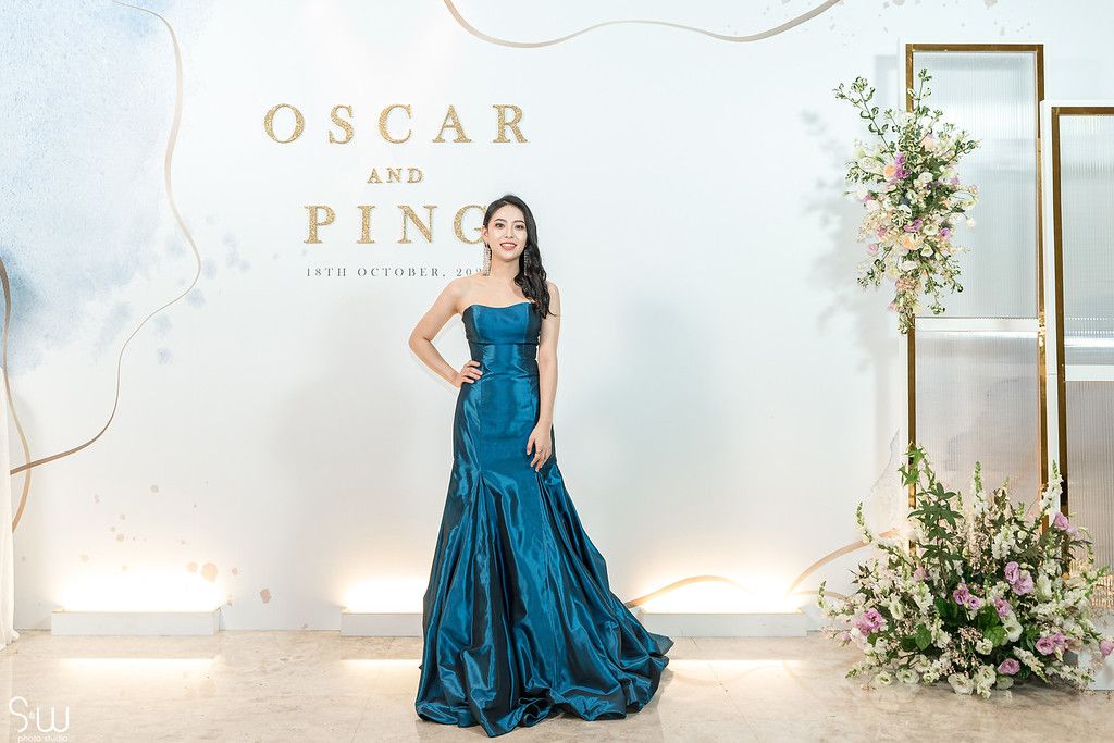 A stunning blue mermaid gown is showcased against an elegant white backdrop with floral decorations.