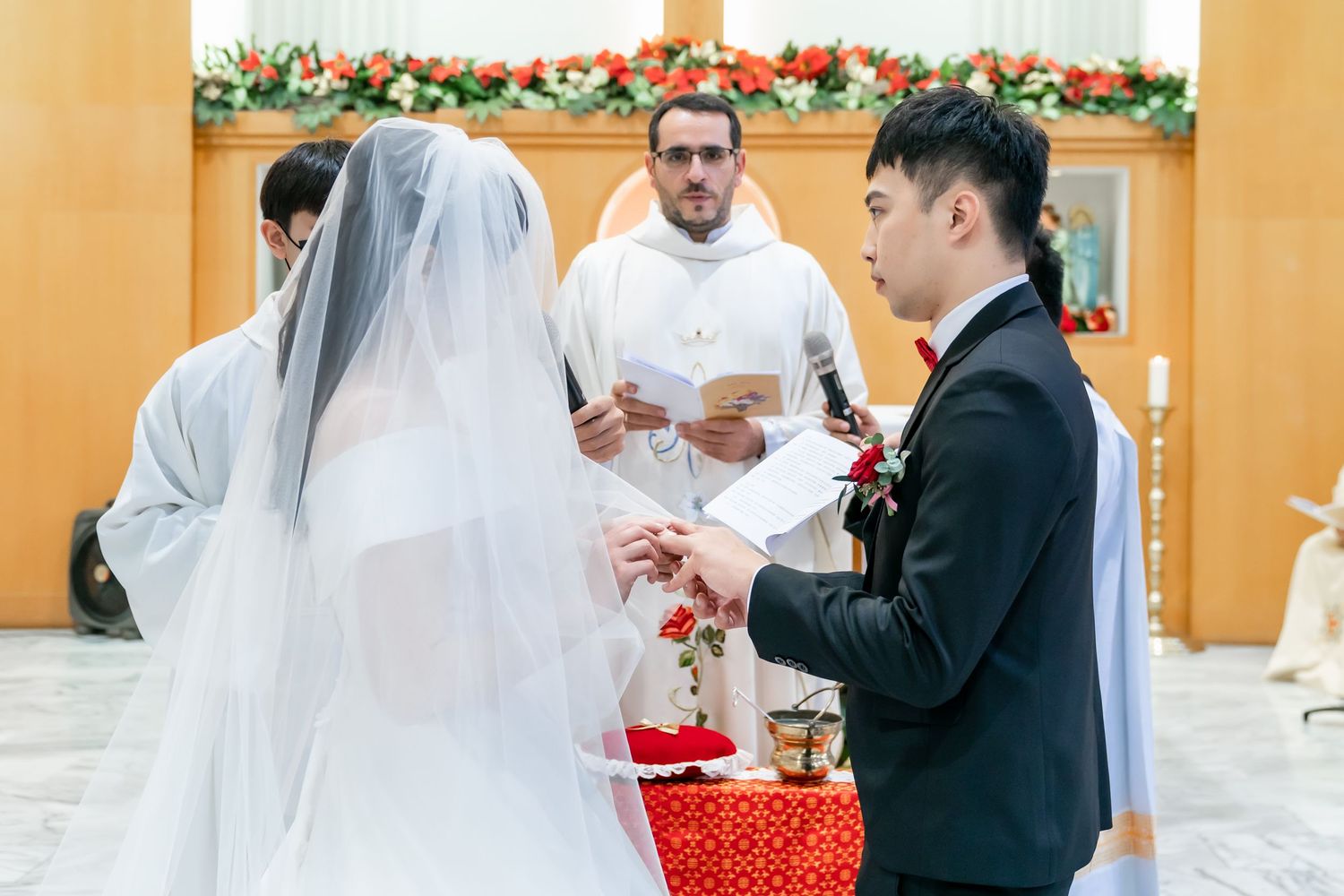 Wedding ceremony with priest officiating as couple exchanges vows near decorated altar.