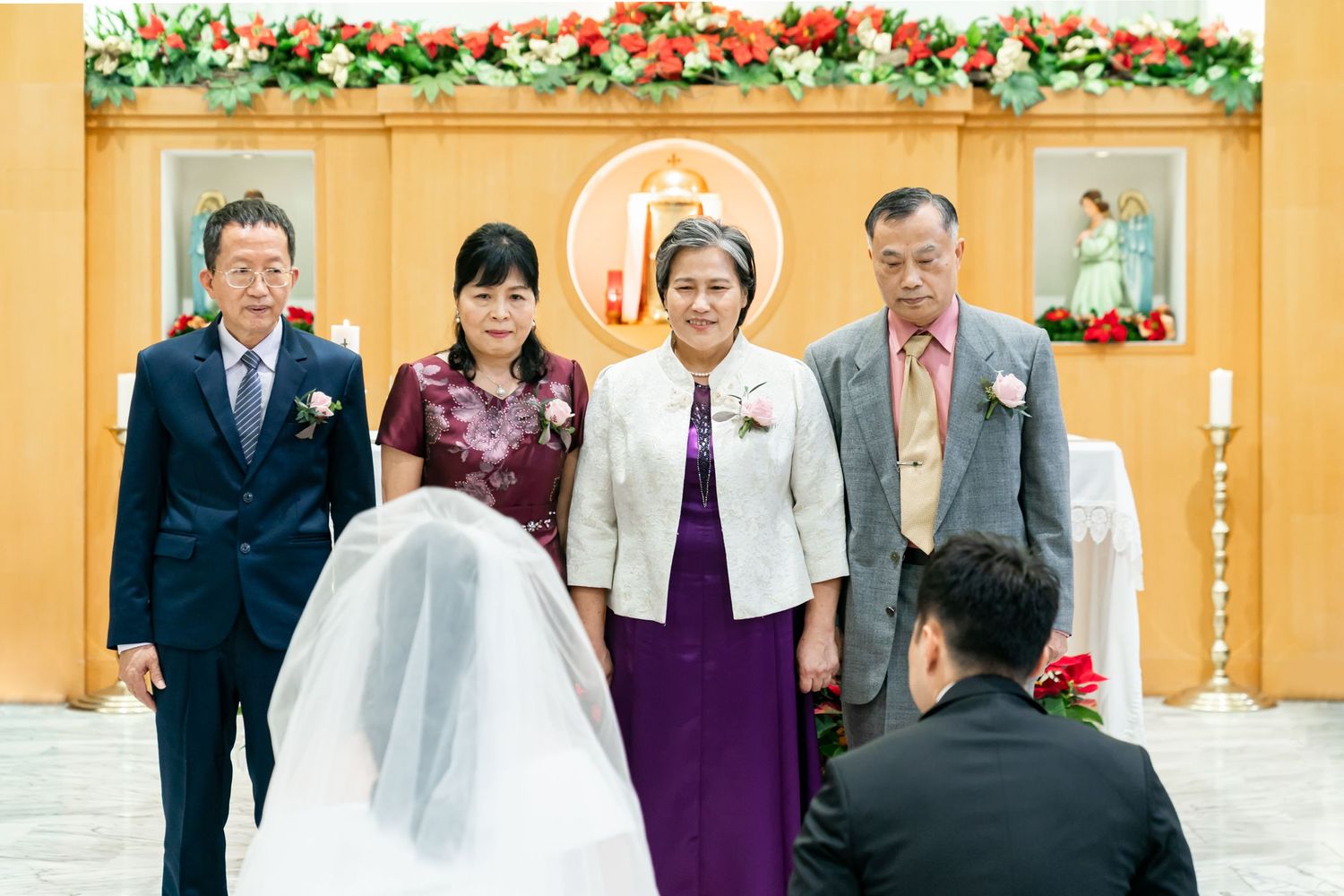 A wedding ceremony group stands at the altar decorated with red and white floral garlands.
