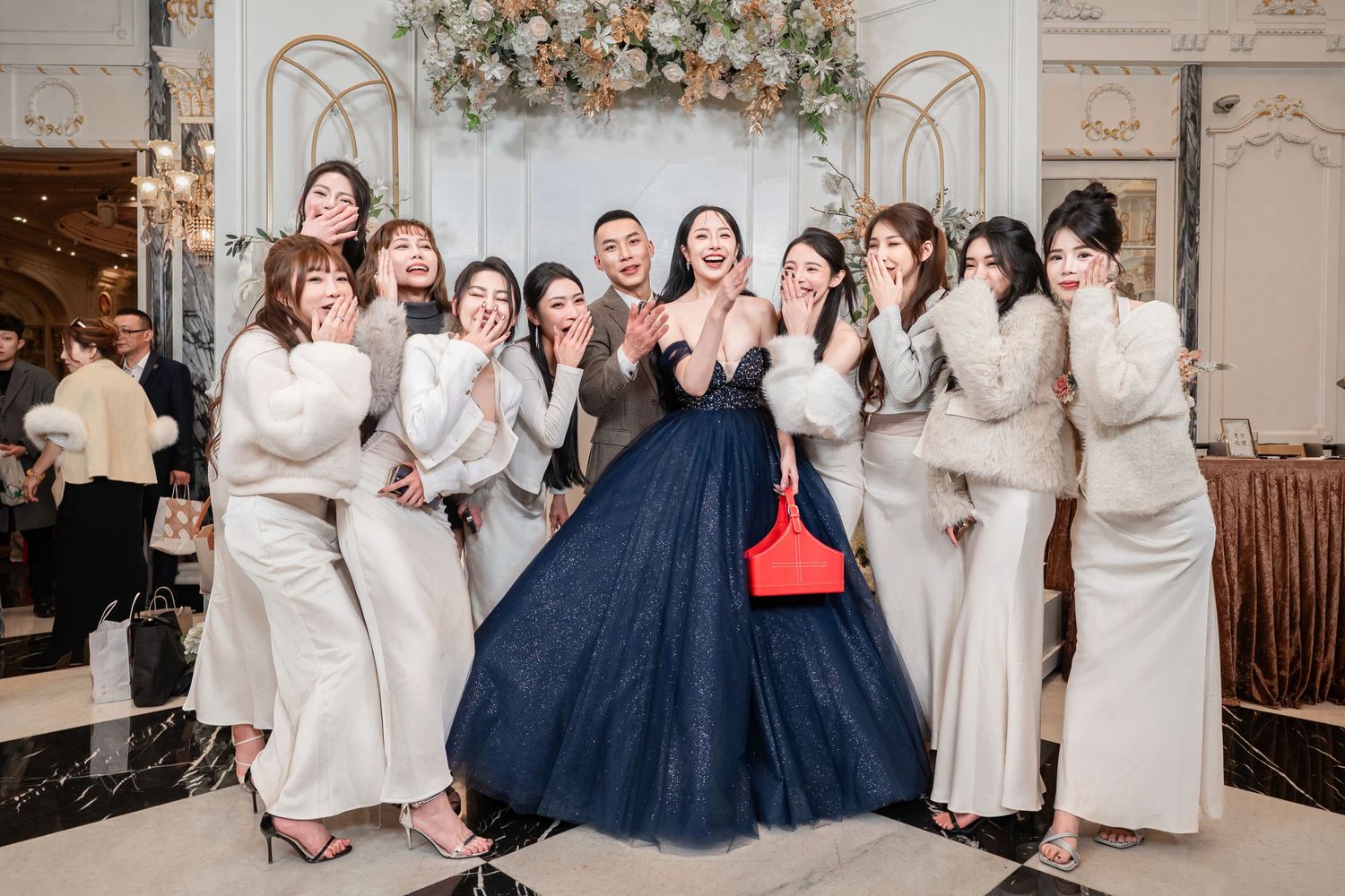 A bride in a navy blue ball gown poses with bridesmaids wearing white dresses at an elegant wedding reception venue.