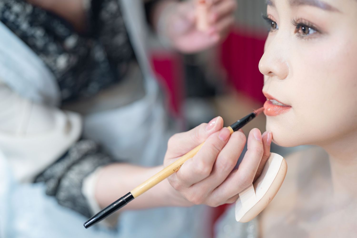 Makeup artist applies lipstick with a professional brush during cosmetic application session.